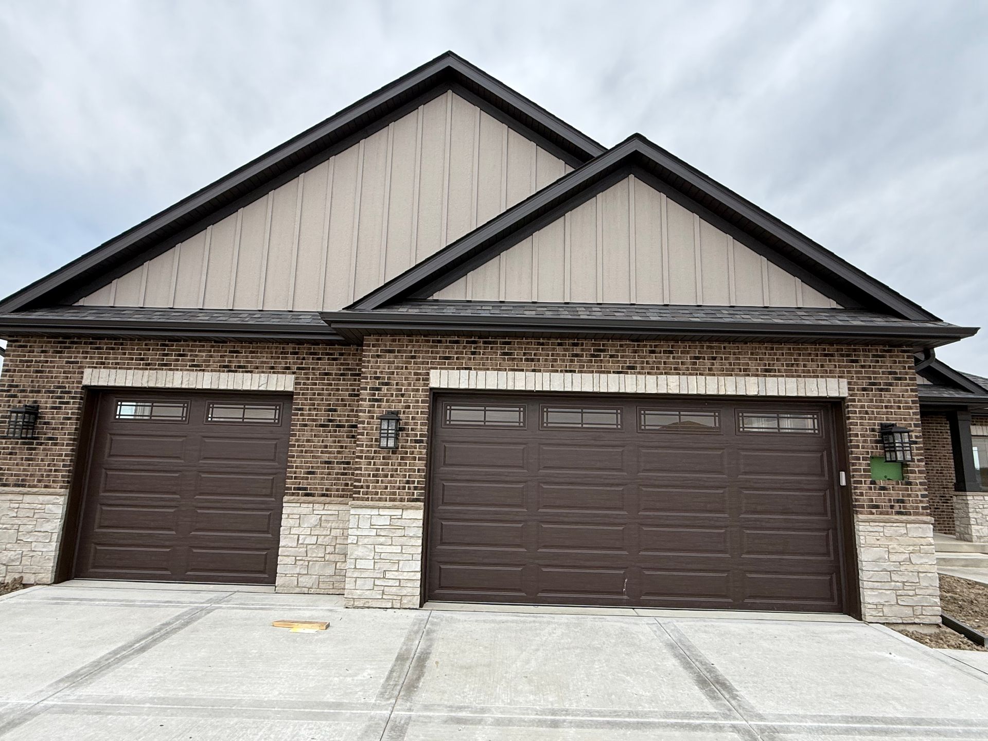 Front view of a two-car brick garage with brown doors and a snow-dusted driveway