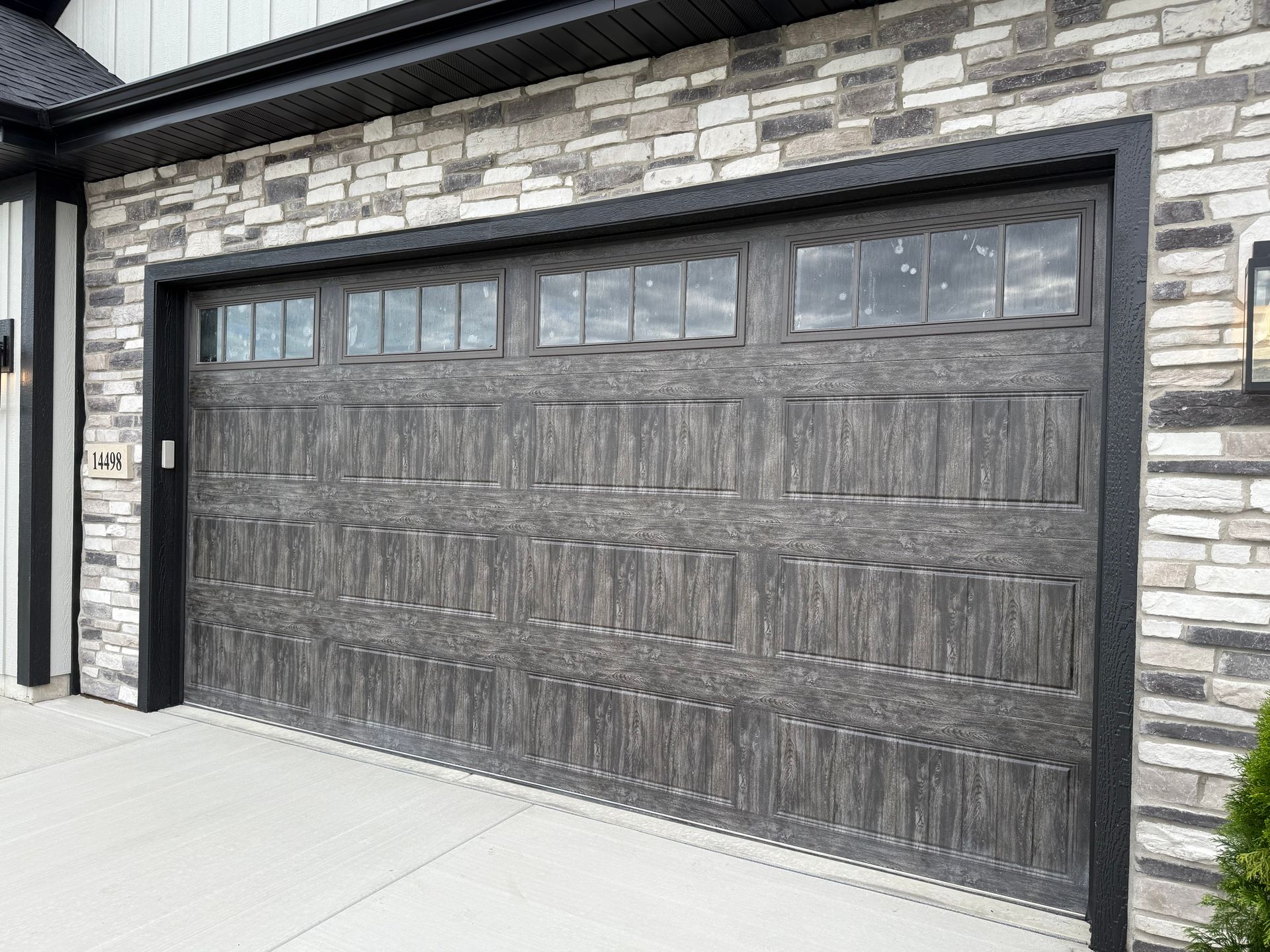 Dark wood-paneled garage door with small windows in a stone exterior wall