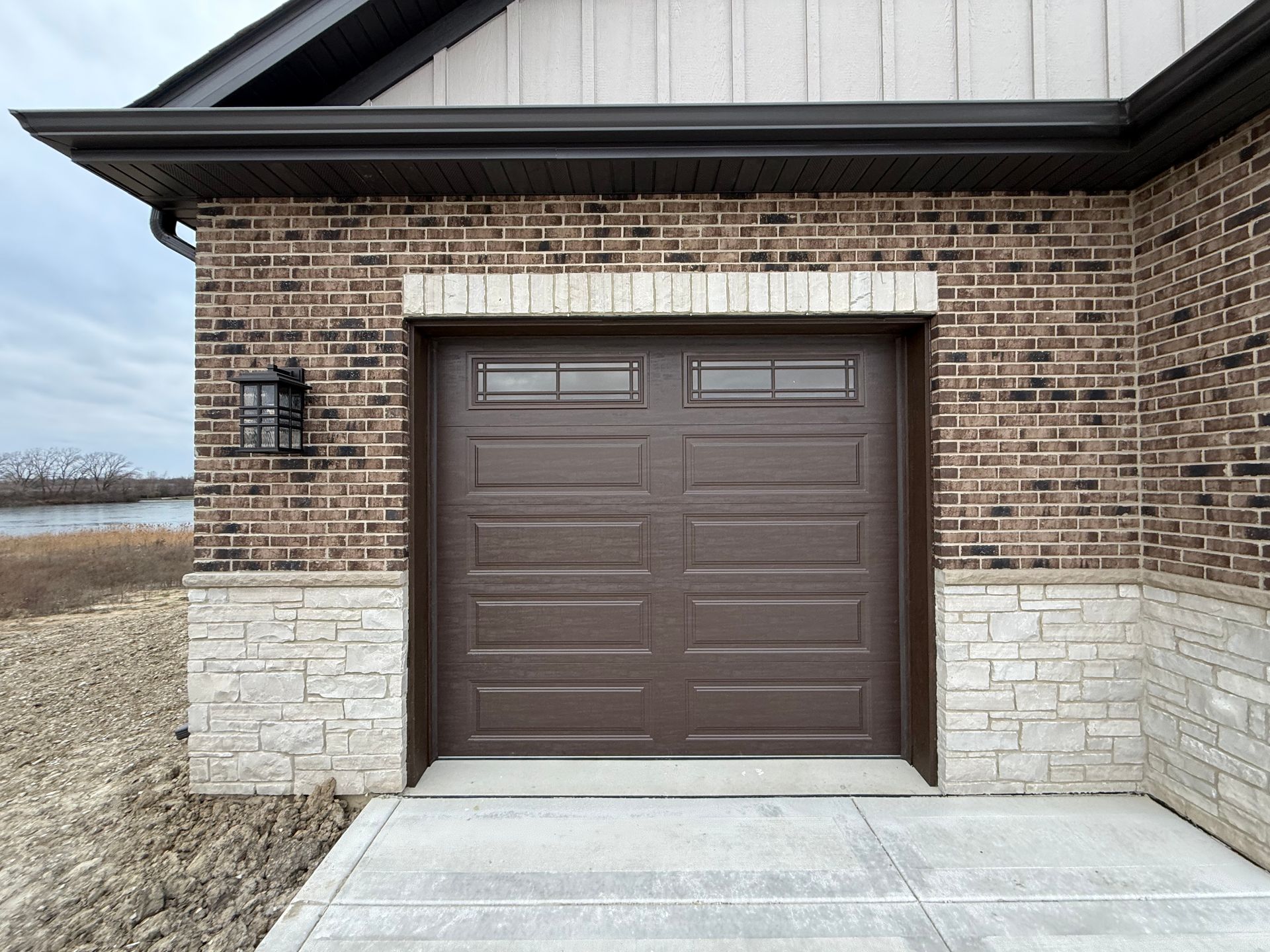 Brown garage door set into a brick house exterior with stone trim and concrete driveway