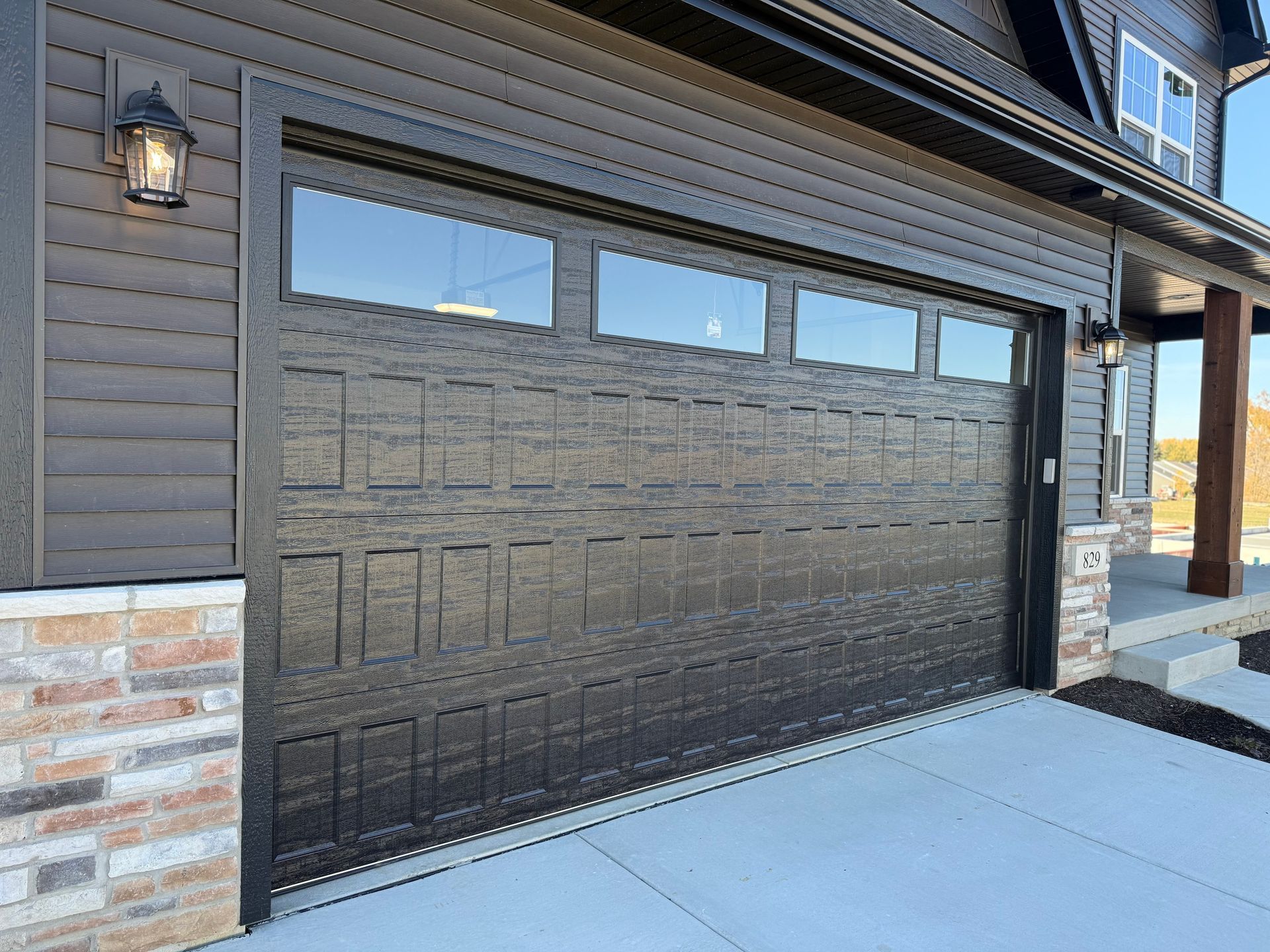 Black garage door on a house exterior with stone accents and a concrete driveway