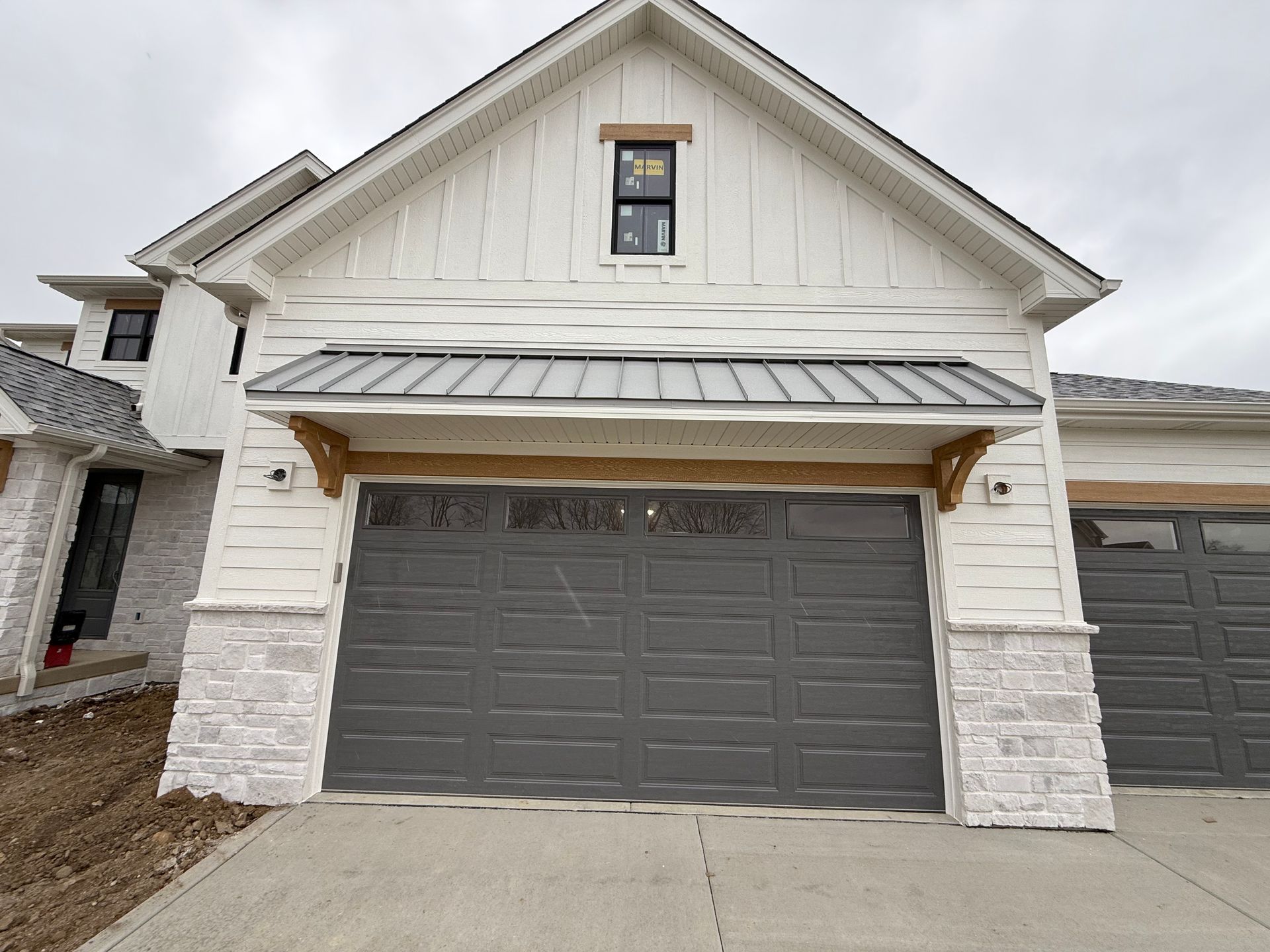 White house exterior with a gray double garage door and stone accents under a gabled roof