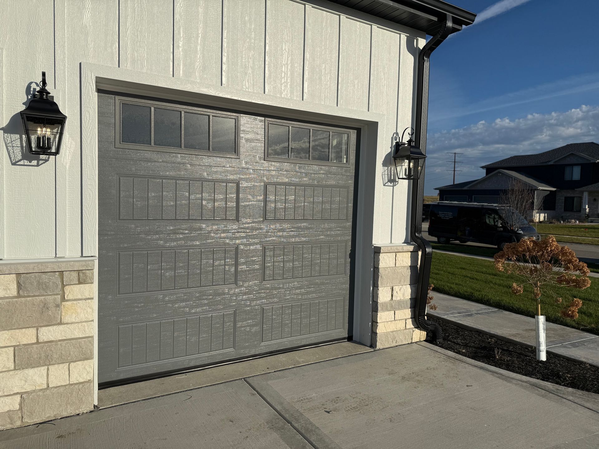 Gray garage door on a white house with stone trim, beside a driveway in a suburban neighborhood.