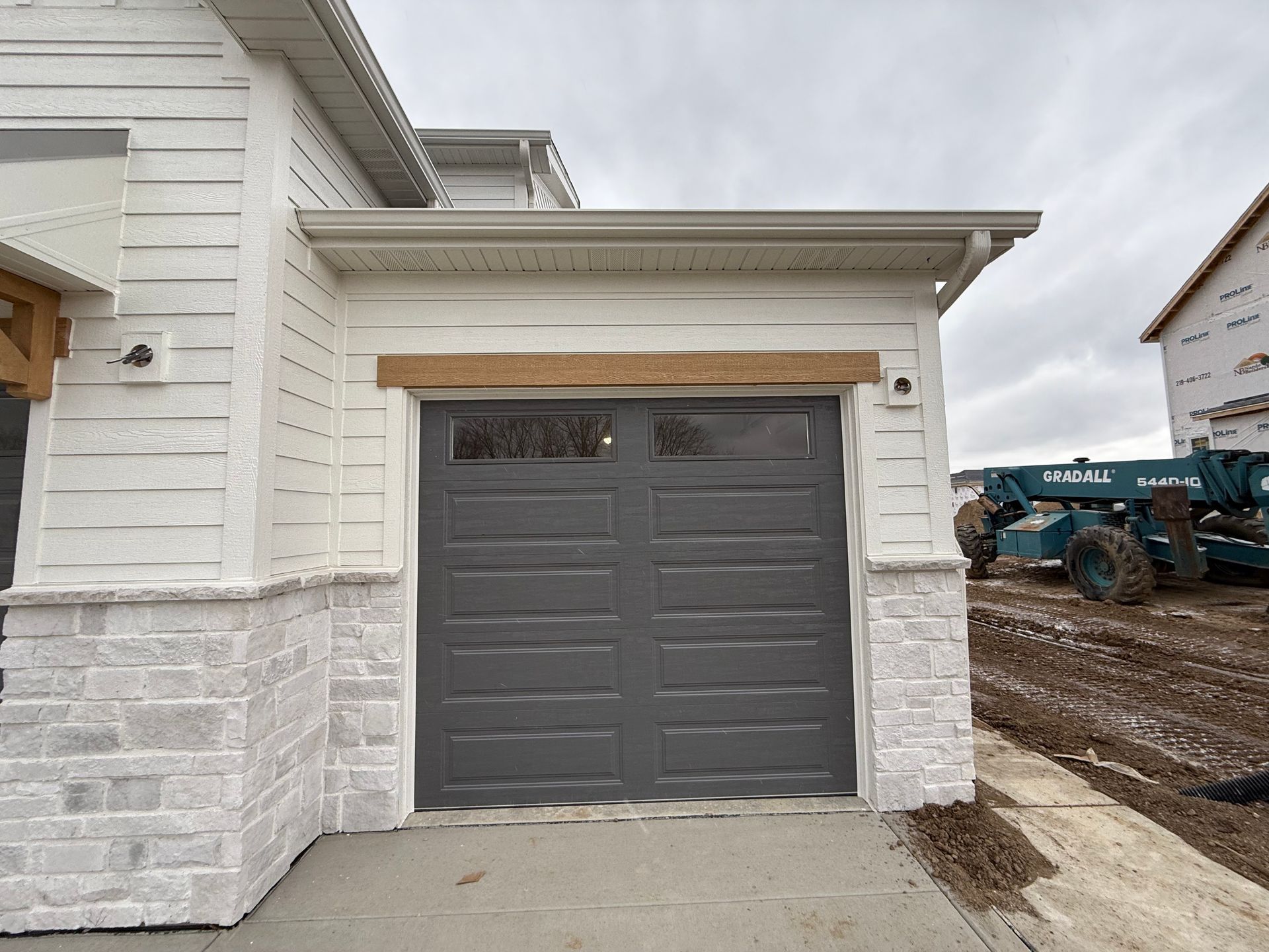 Gray garage door on a white house exterior with stone base and construction equipment nearby