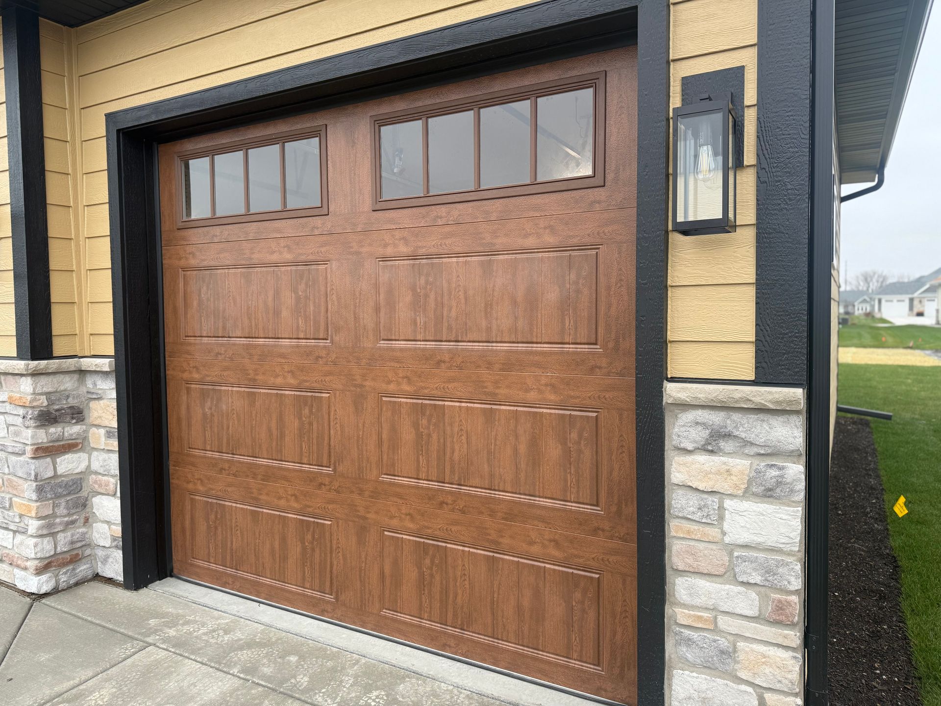 Wooden garage door with small windows set in a stone and beige house exterior