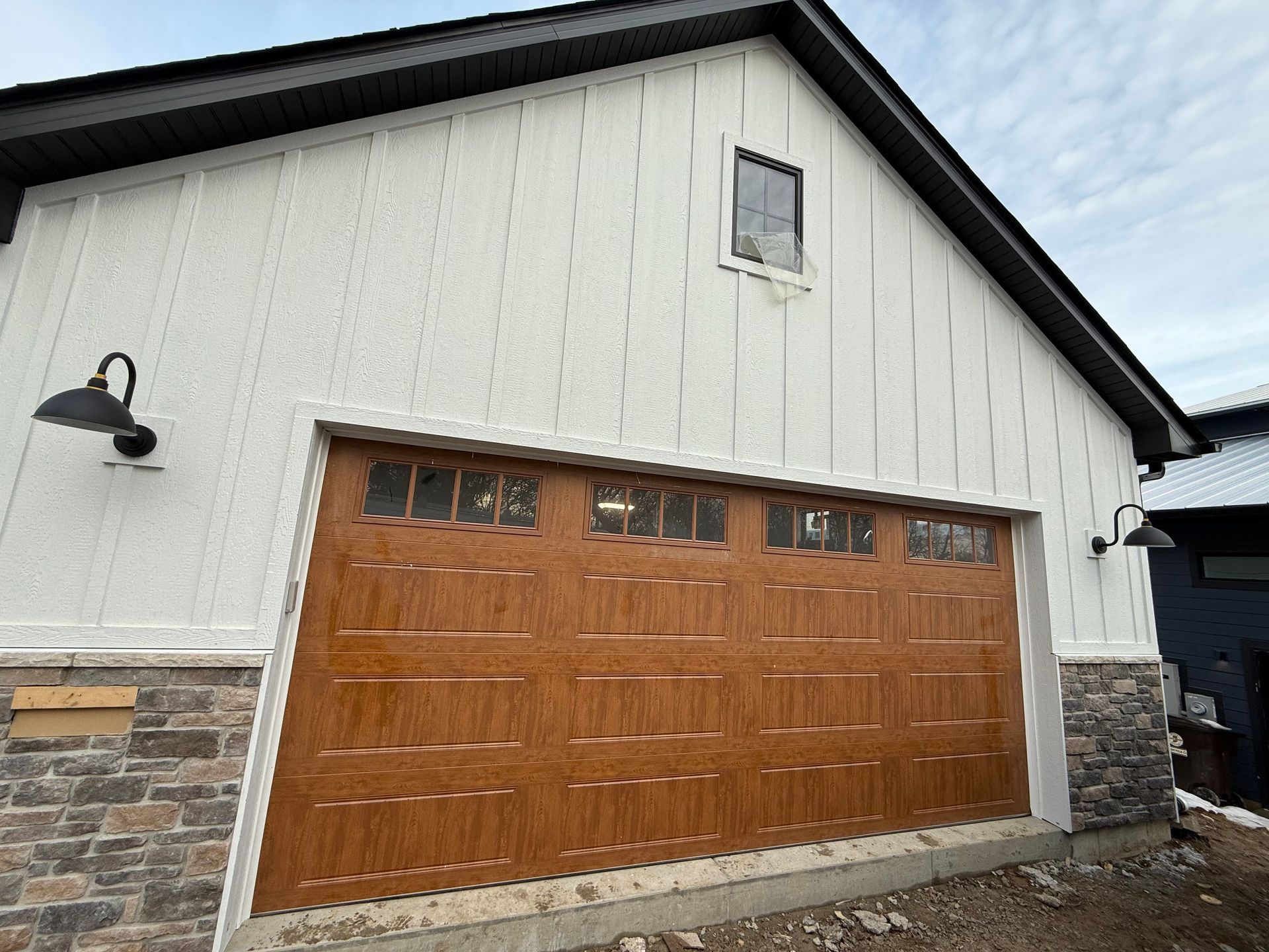 White garage with a brown wood-paneled door on a stone-and-siding house under an overhang.