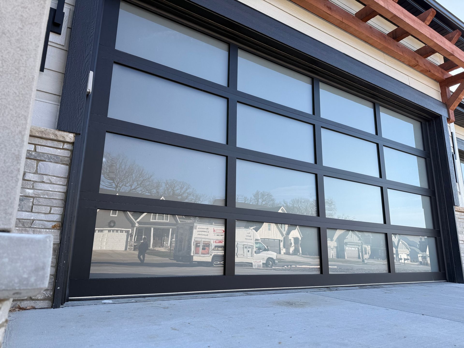 Modern building facade with large black-framed glass garage doors and stone exterior, viewed from the sidewalk