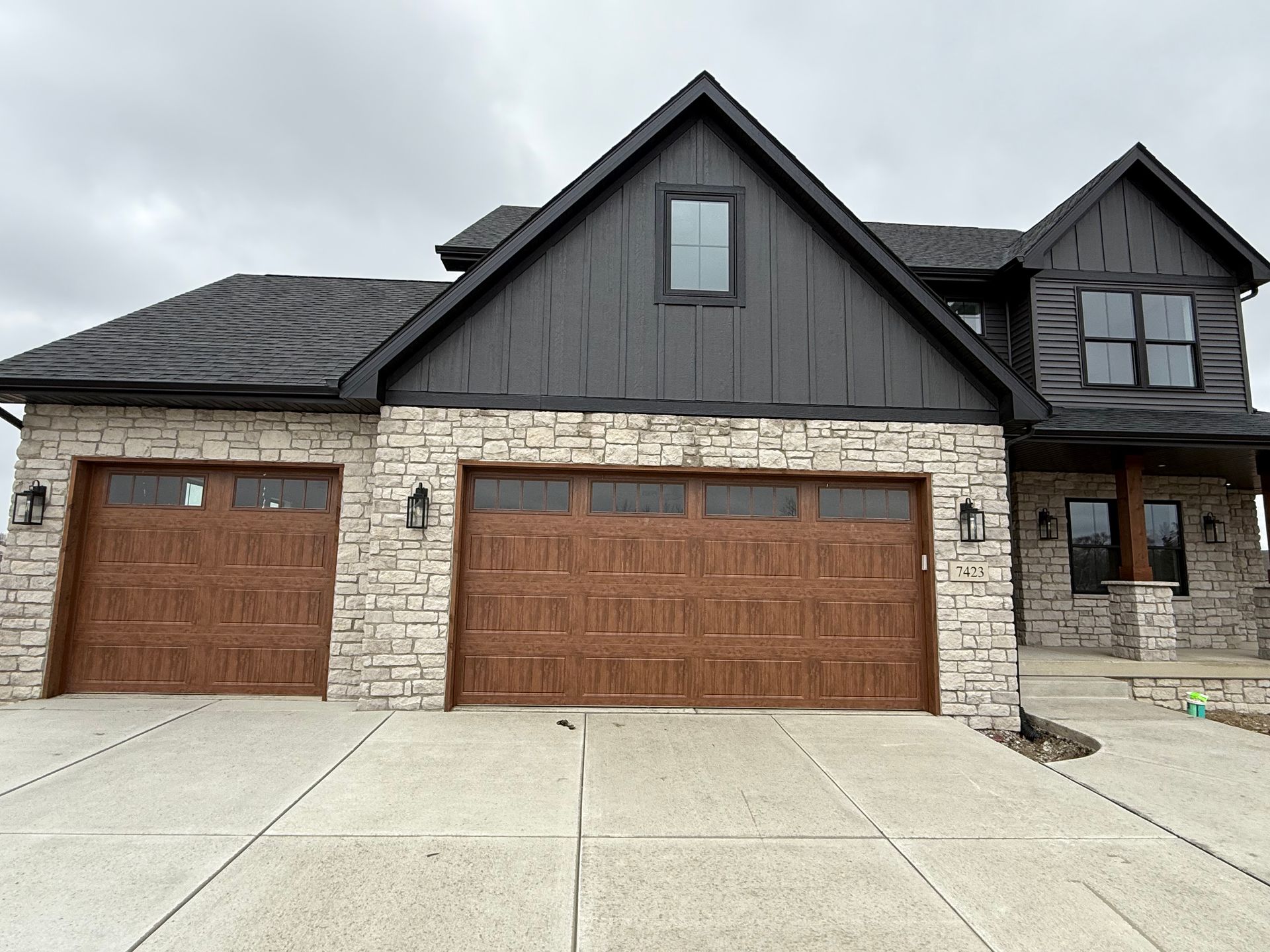 Suburban house exterior with stone facade, dark gray siding, and two wooden garage doors