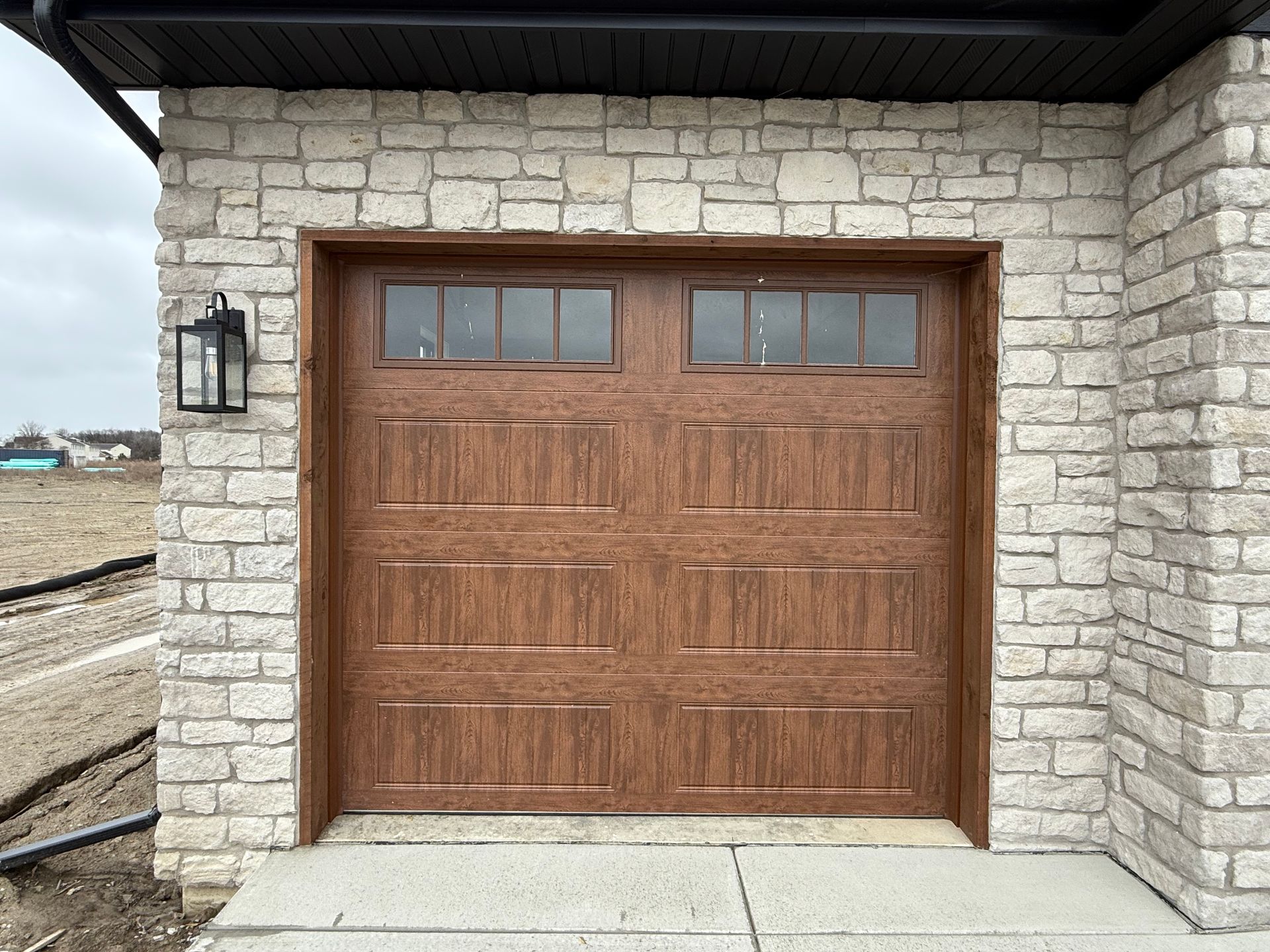 Wooden garage door set in a stone exterior wall with a black lantern light on the left.