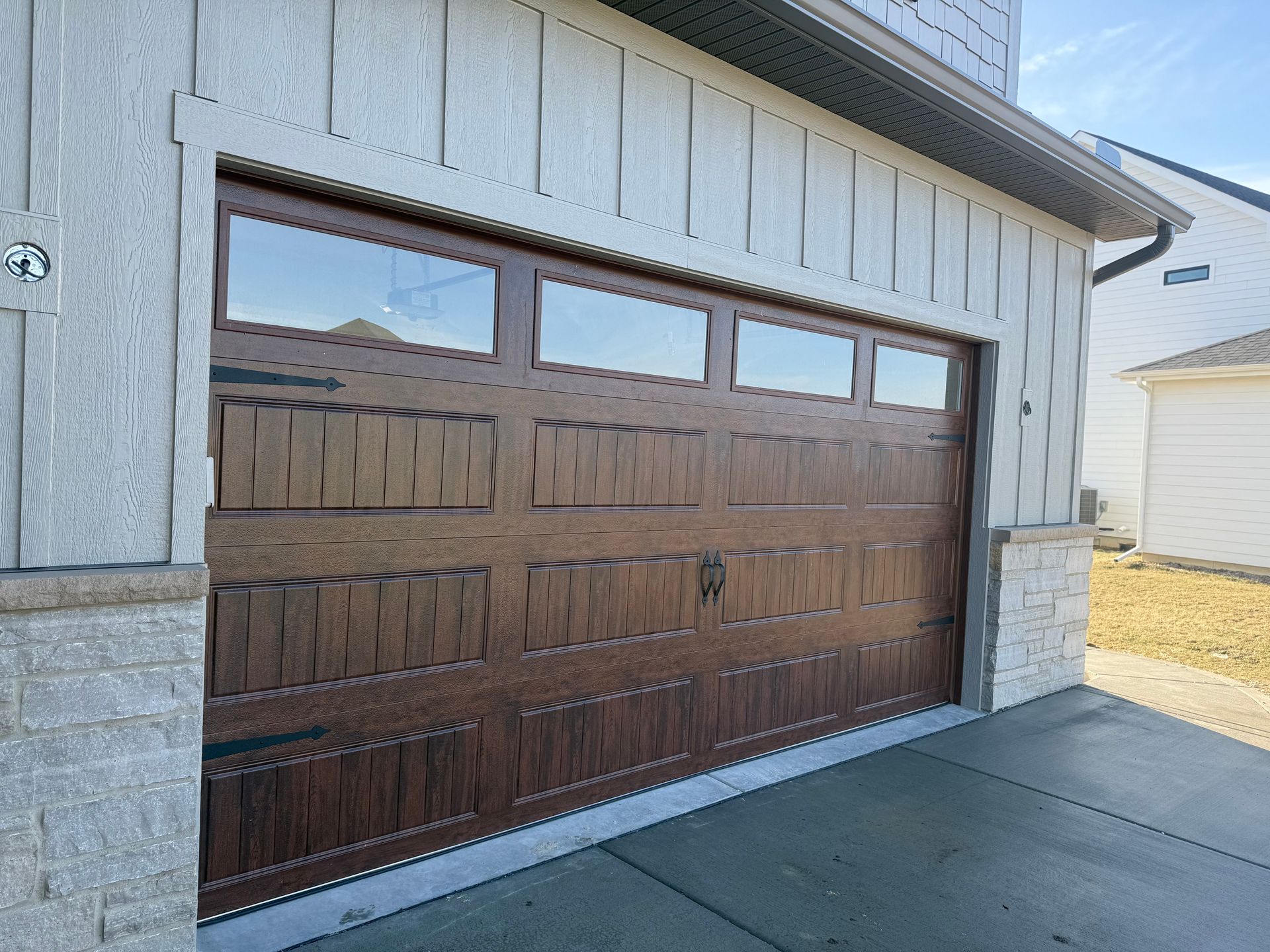 Wooden garage door with windows on a stone-and-siding house, beside a driveway