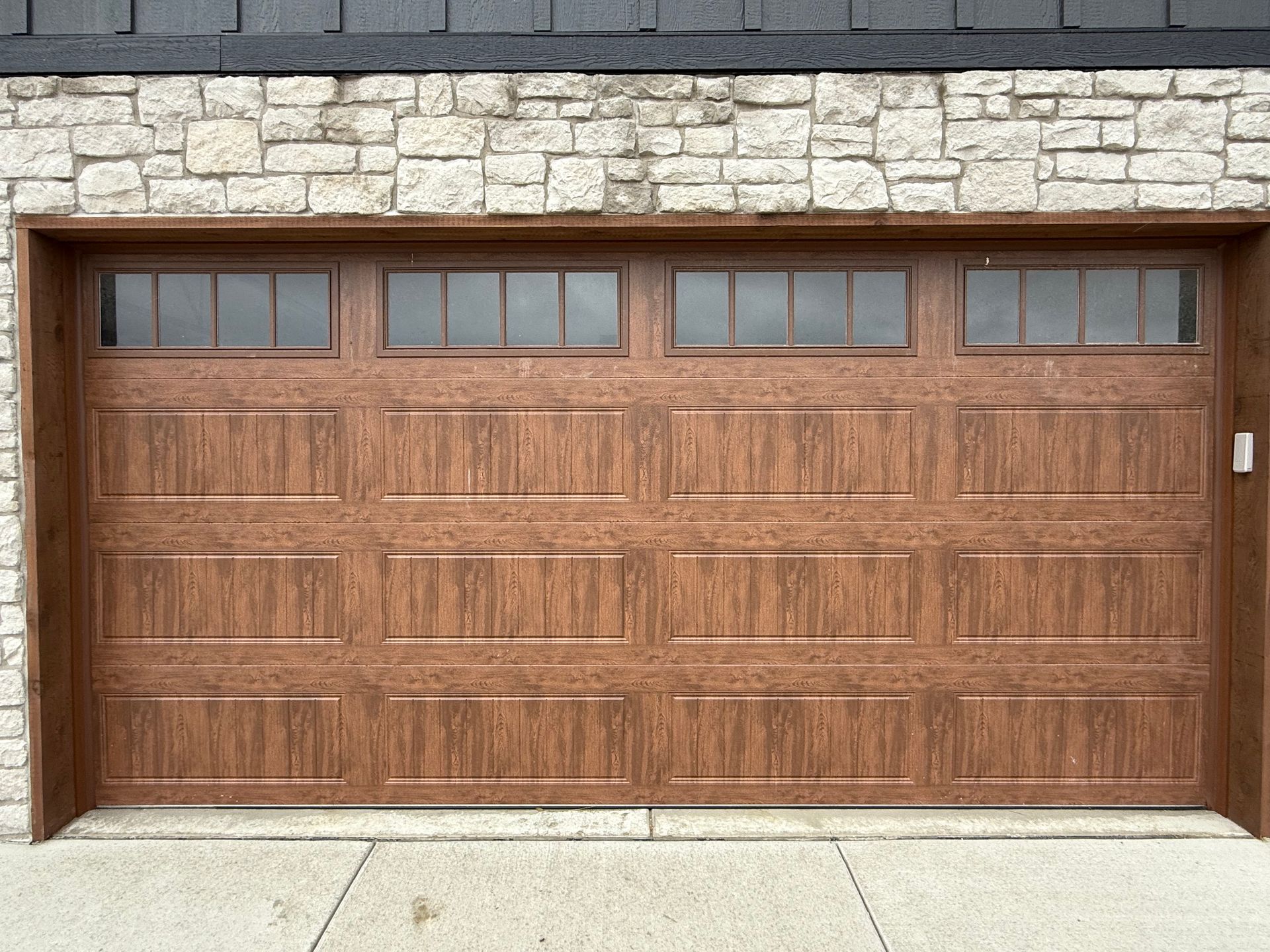 Wooden two-car garage door with small windows set in a stone exterior wall