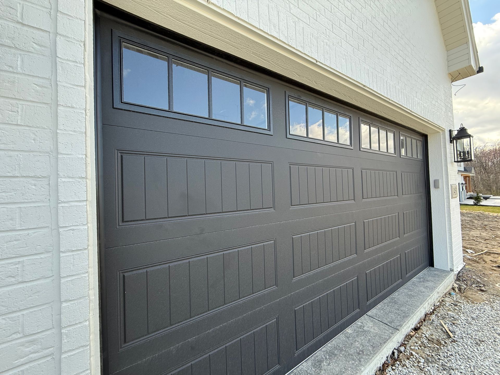 Gray sectional garage door with small windows on a white house exterior
