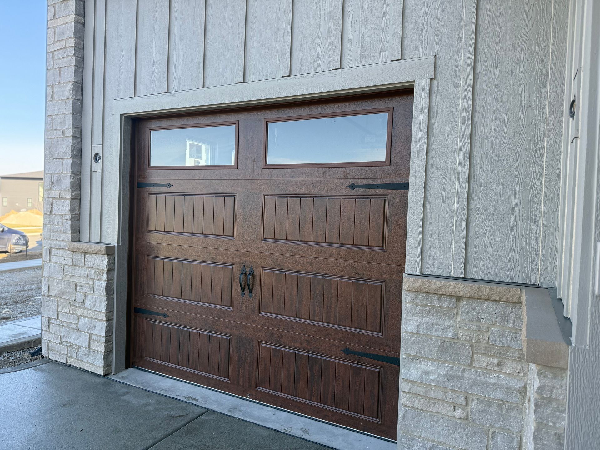 Brown paneled garage door set into a light gray stone and siding exterior wall