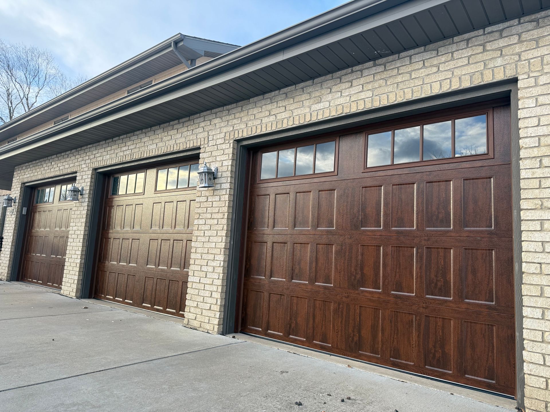 Three wooden garage doors on a brick house with a concrete driveway