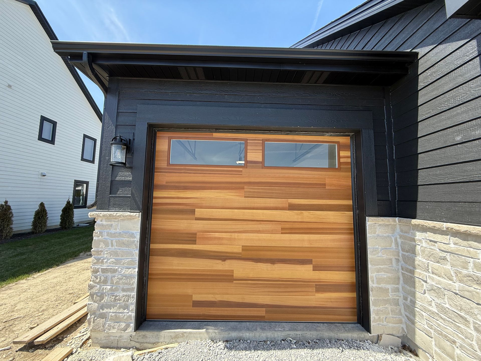 Wooden garage door with small windows on a modern house exterior, framed by stone and dark siding.