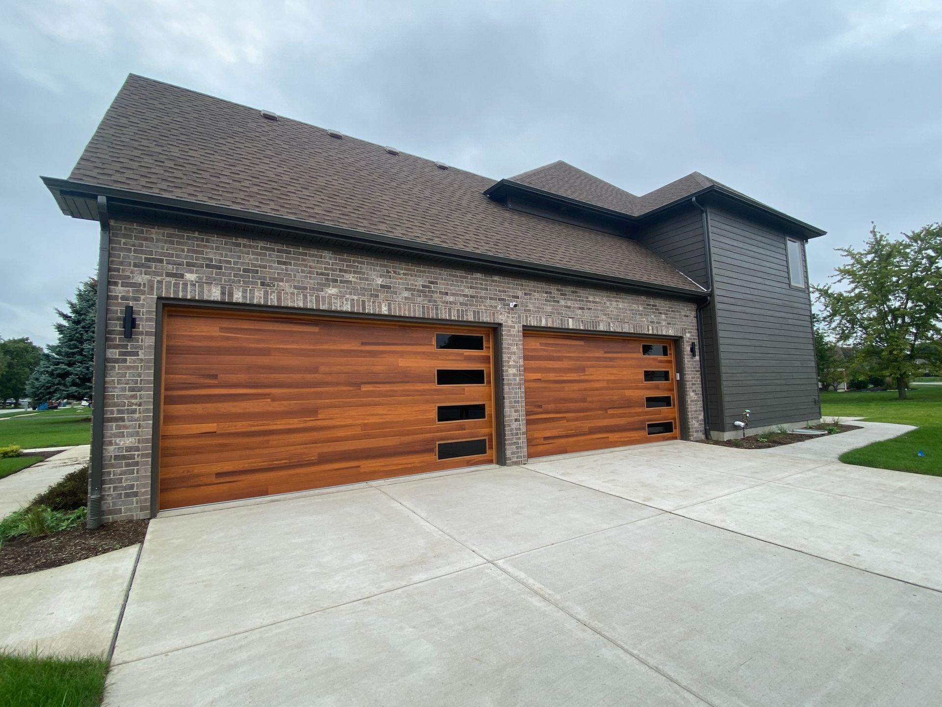Modern two-car garage with wood doors, brick exterior, and concrete driveway under an overcast sky