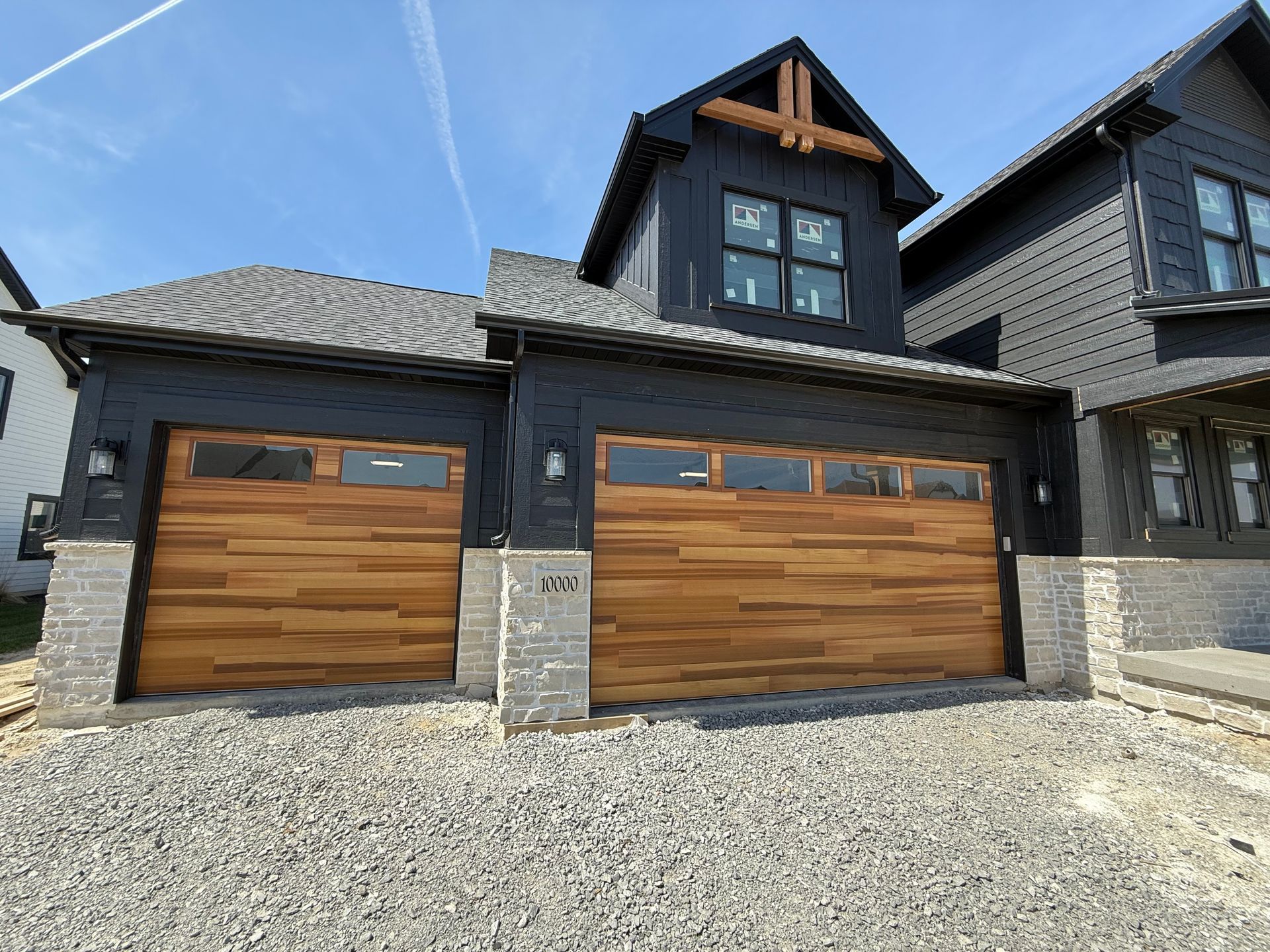 Modern house exterior with two wooden garage doors and a gravel driveway
