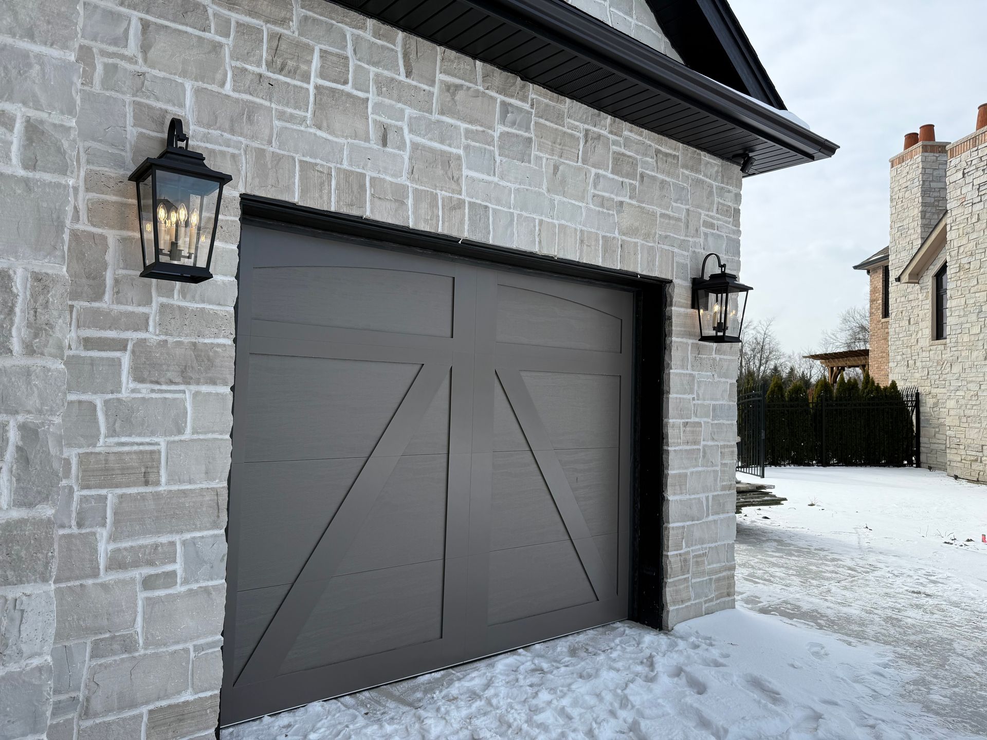 Gray garage door on a stone house beside a snow-covered driveway