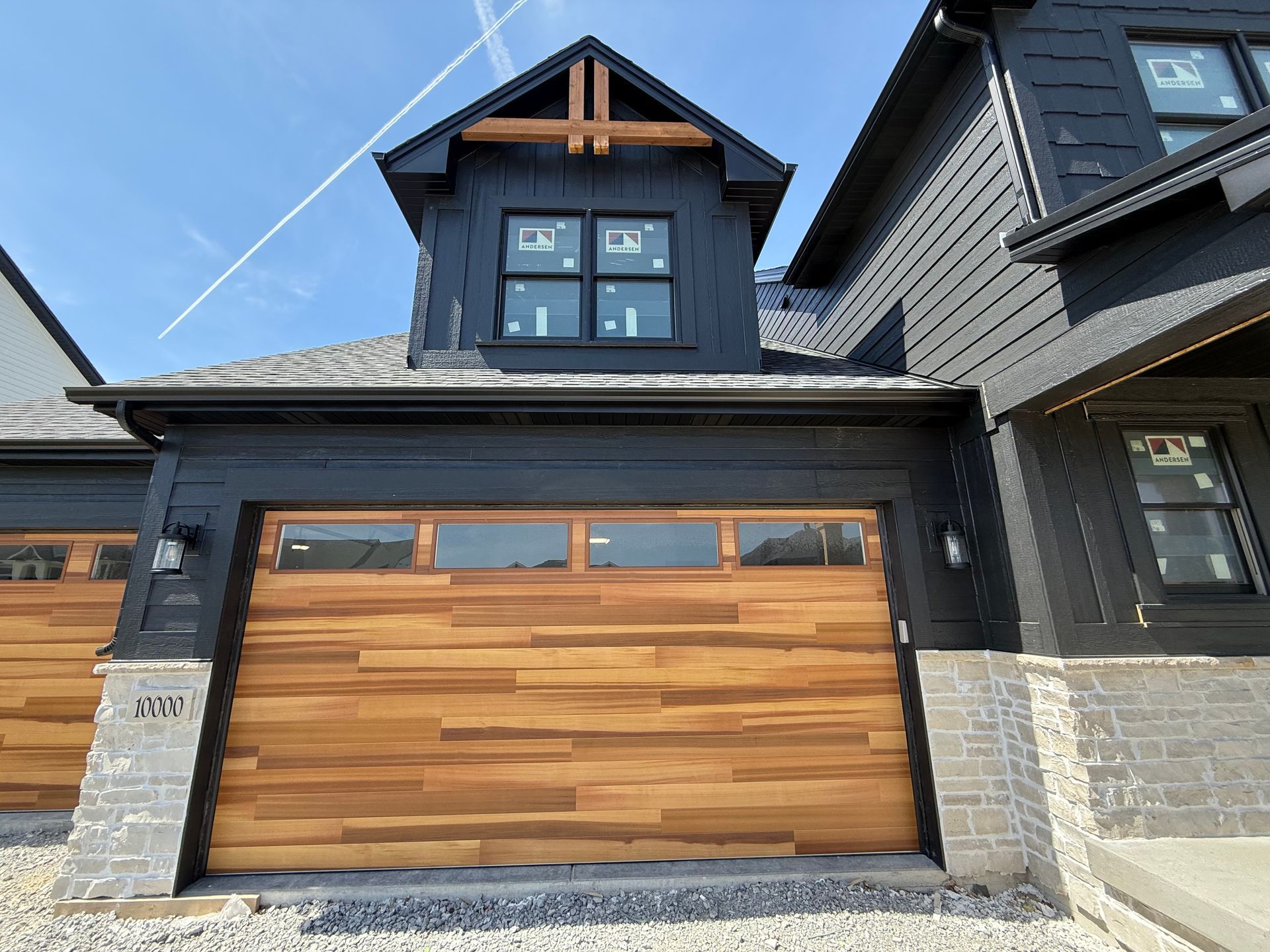 Modern black house exterior with wood garage door and dormer window under blue sky