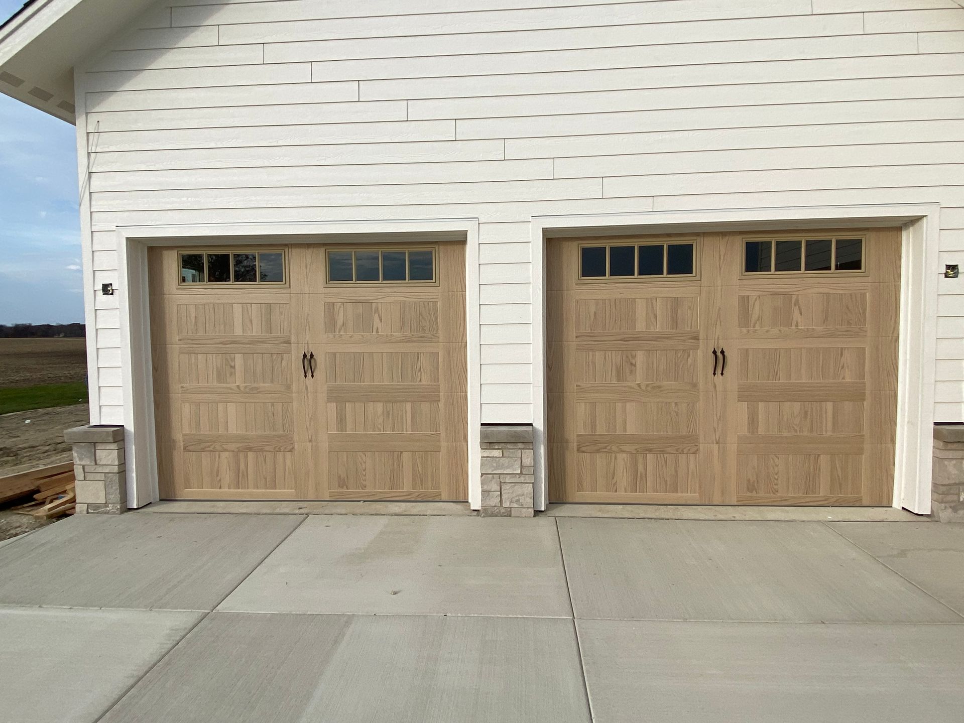 Two tan wooden garage doors on a white house exterior with a concrete driveway