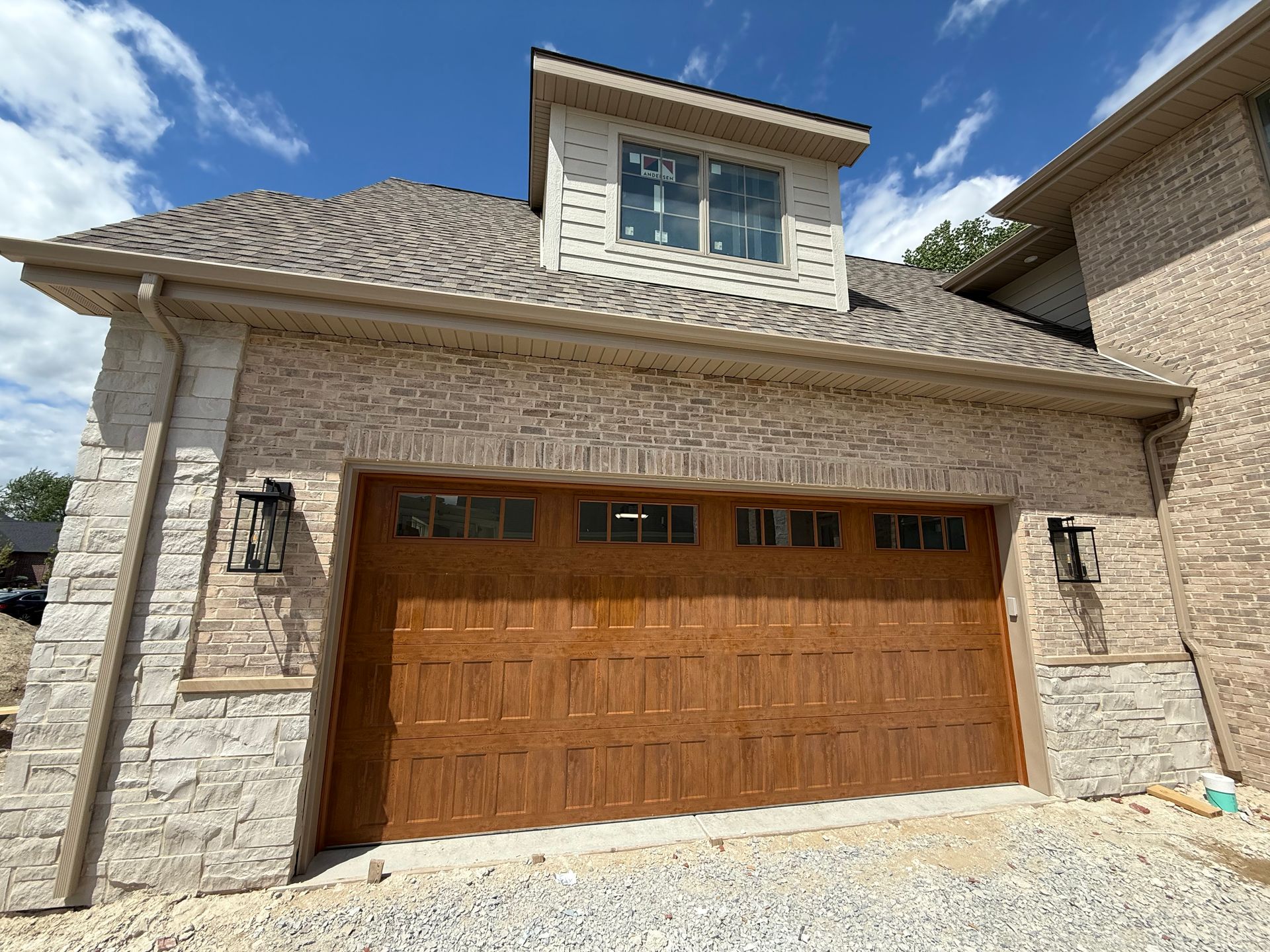 Stone house exterior with a two-car wooden garage door and dormer windows under a cloudy sky