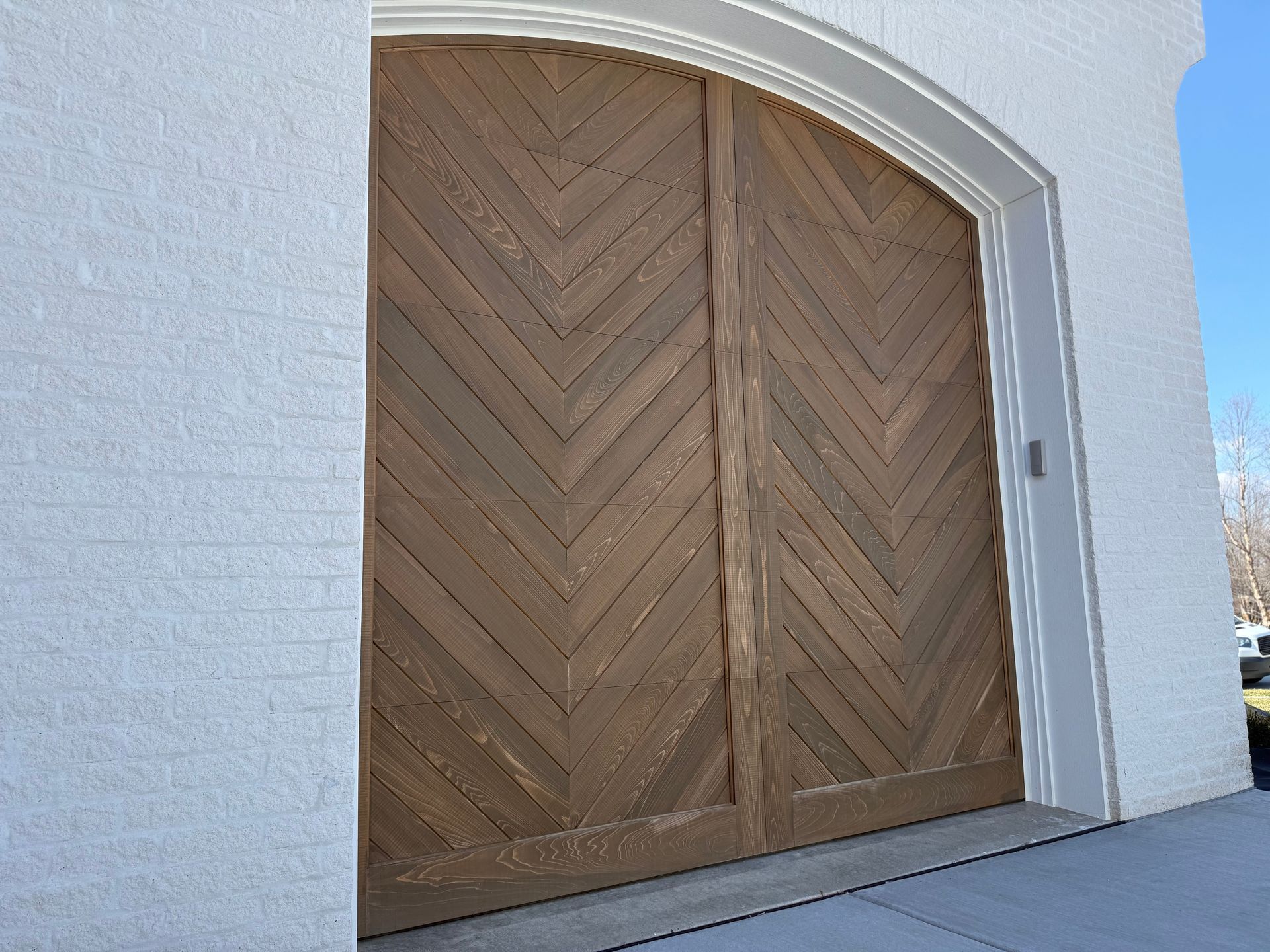Large arched wooden double doors set in a white stucco wall under blue sky