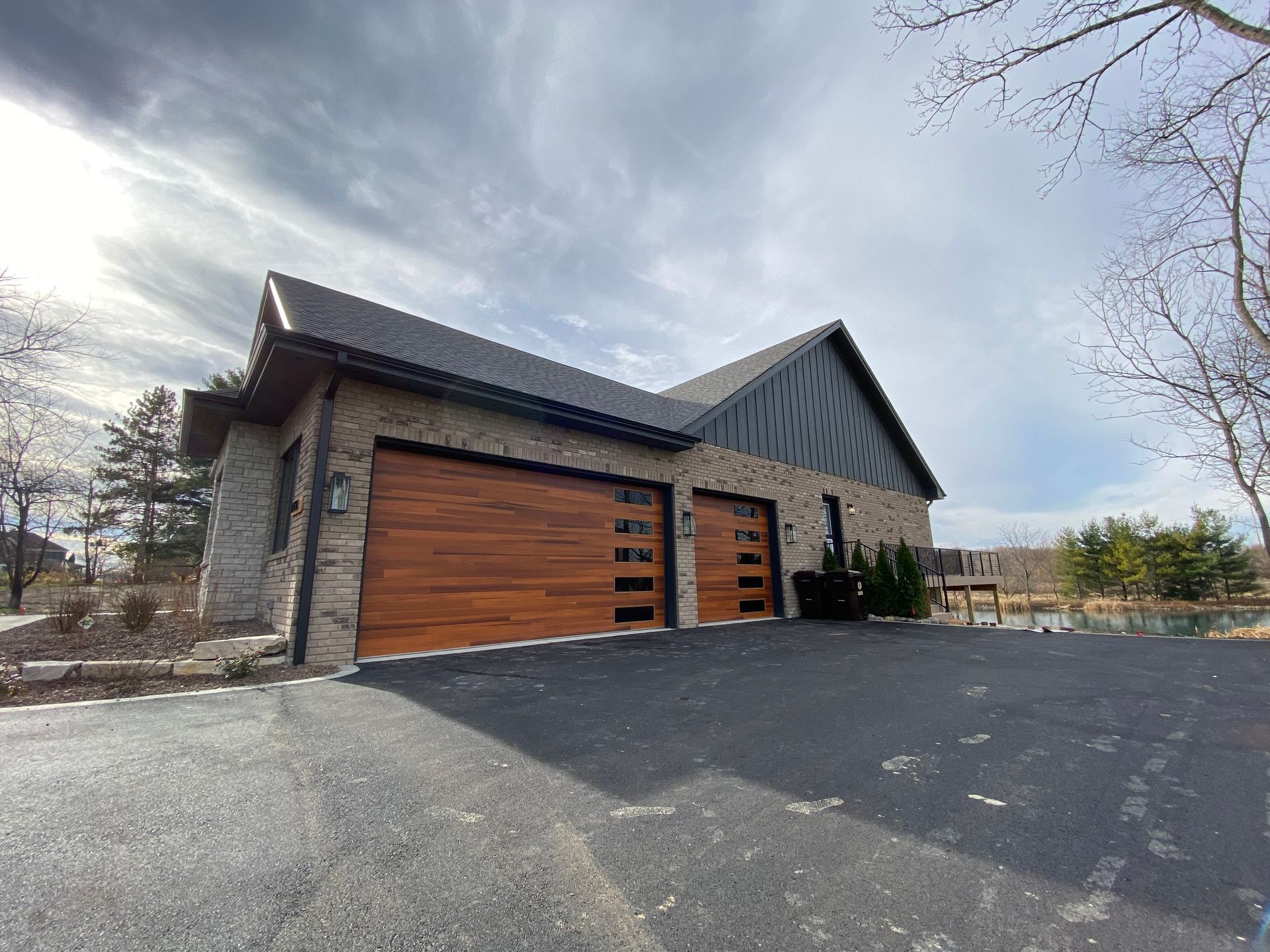 Modern stone house with wood garage doors and a large driveway under a bright sky