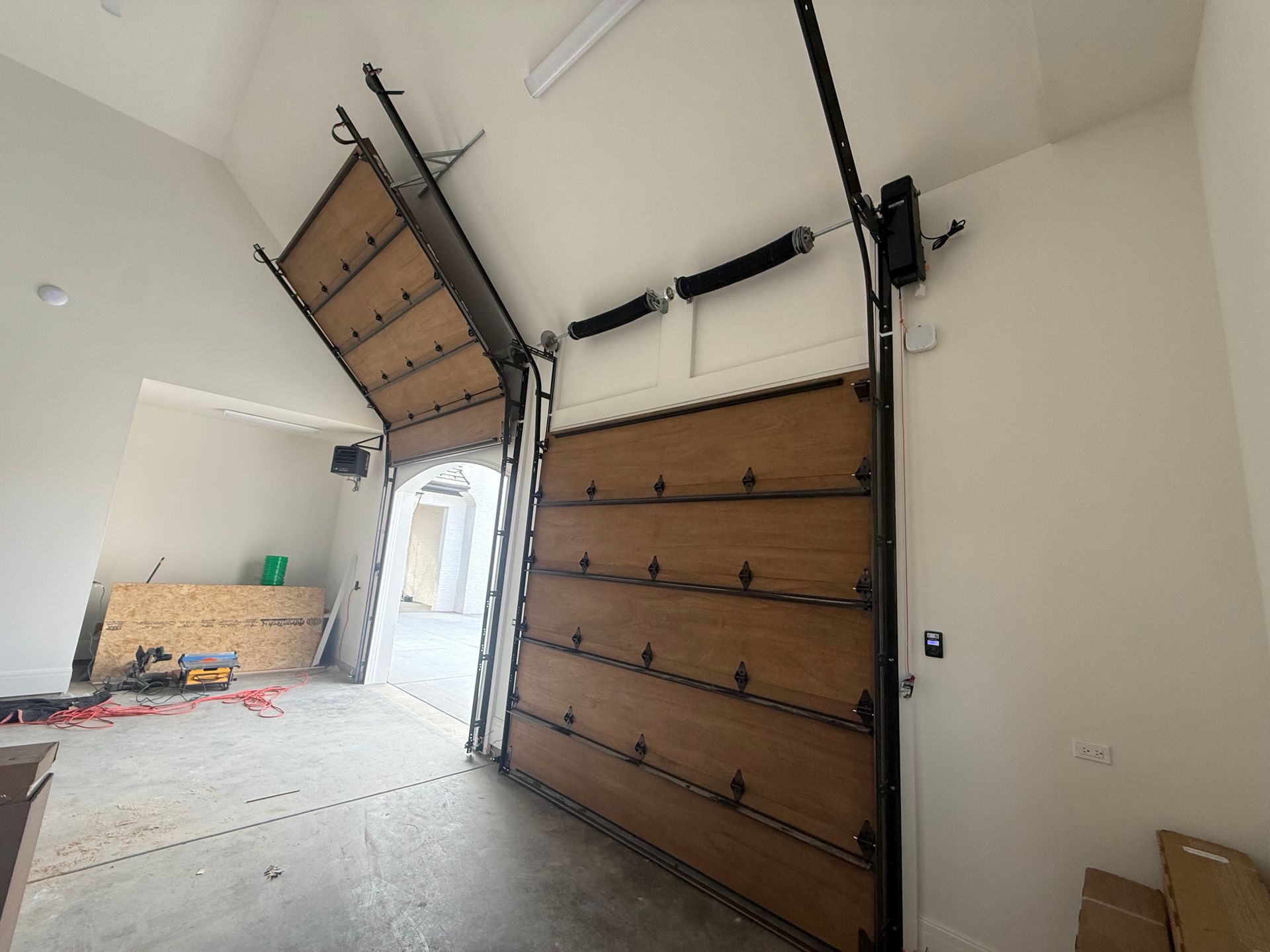 Open garage door with wooden panels and a side entrance in a white interior.