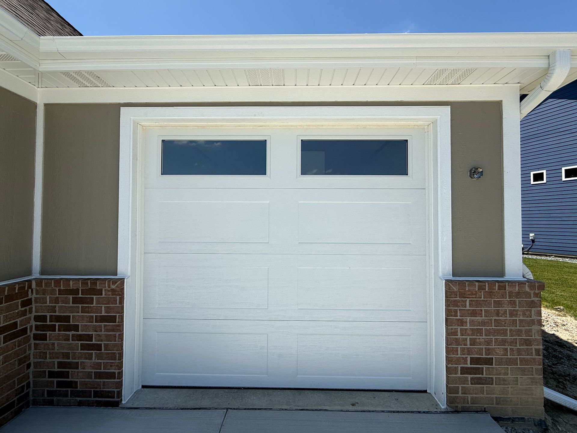 White double garage door with two small windows, framed by brick pillars on a house exterior.