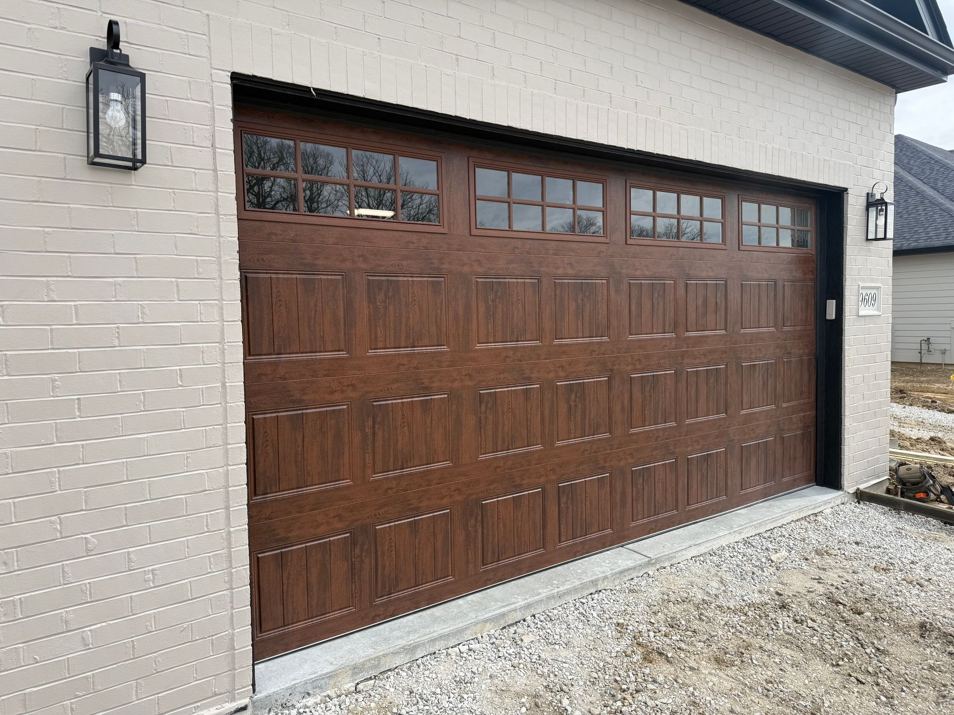 Brown wooden garage door on a white brick house with a gravel driveway.