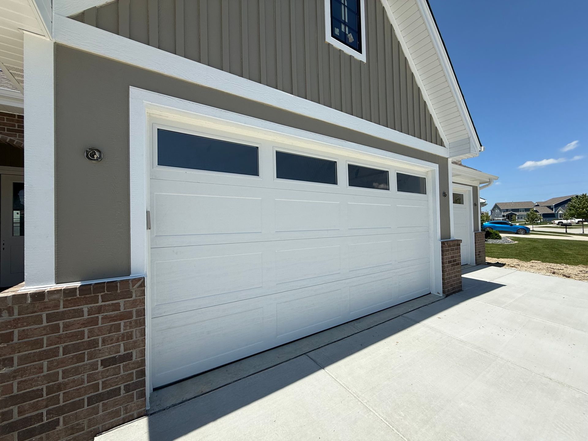 White garage door on a house with brick trim and a concrete driveway on a sunny day