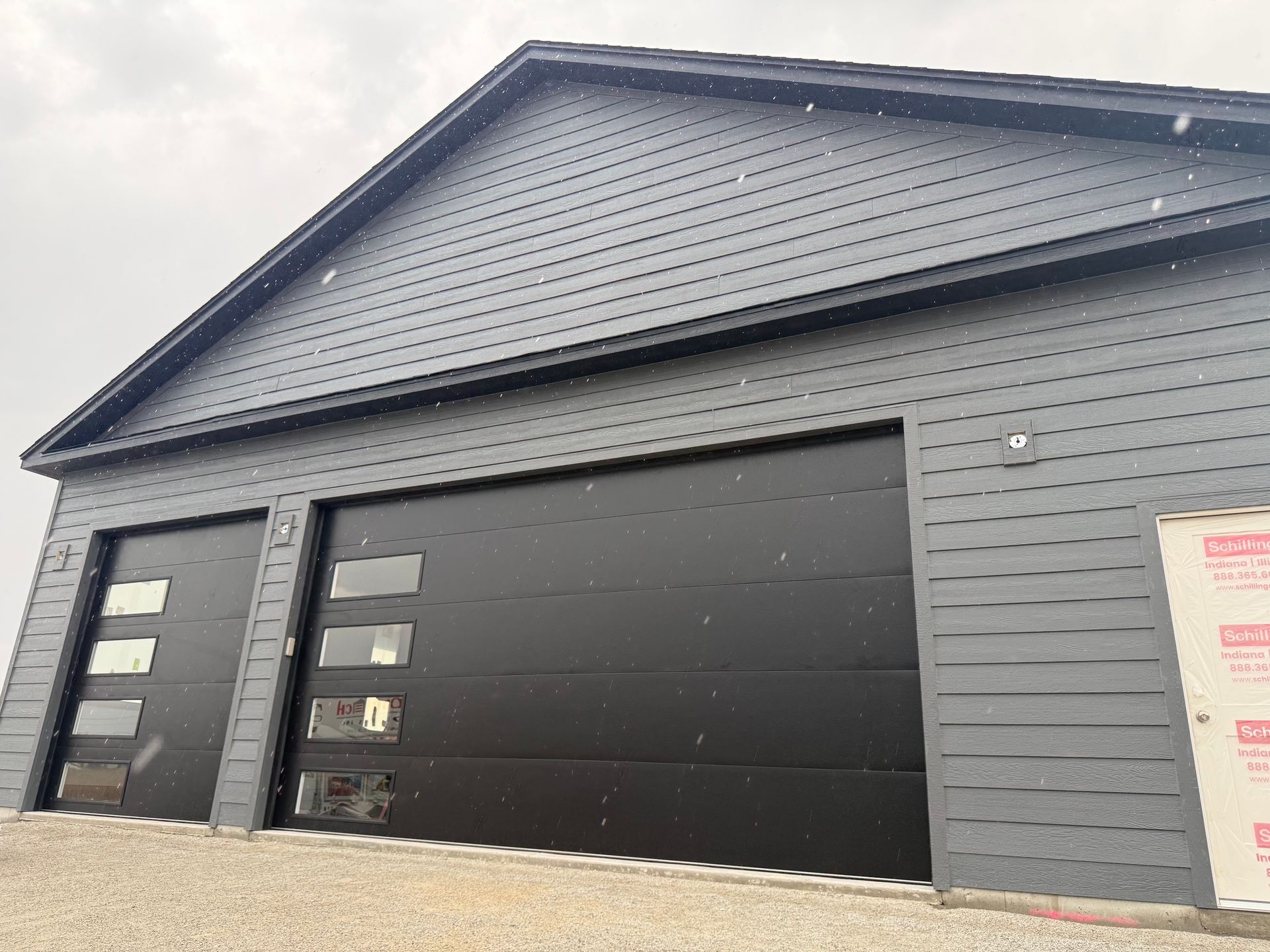 Black garage with horizontal siding and a large dark door under a peaked roof.