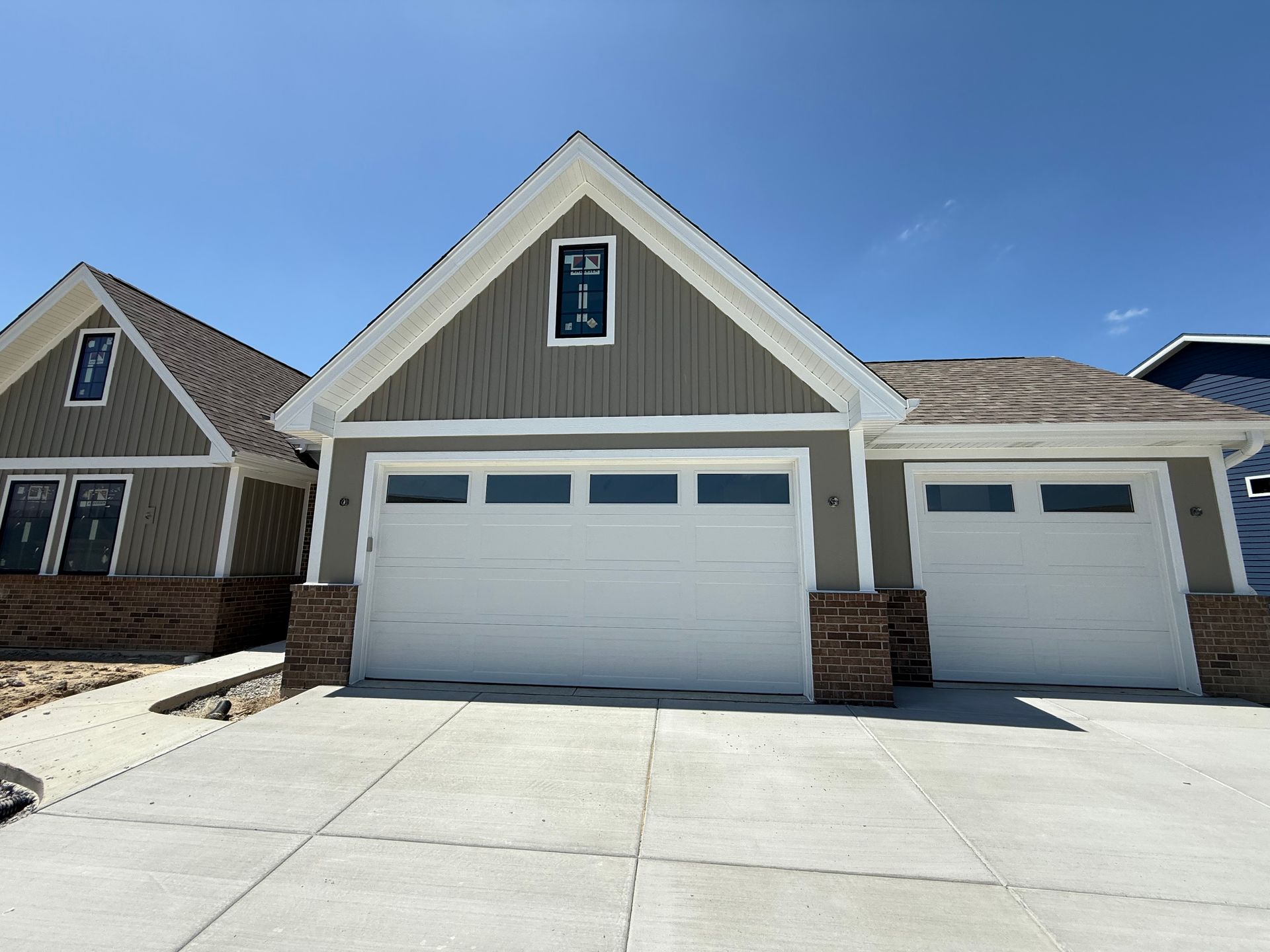 Suburban house with white garage doors, stone accents, and blue trim under a clear sky