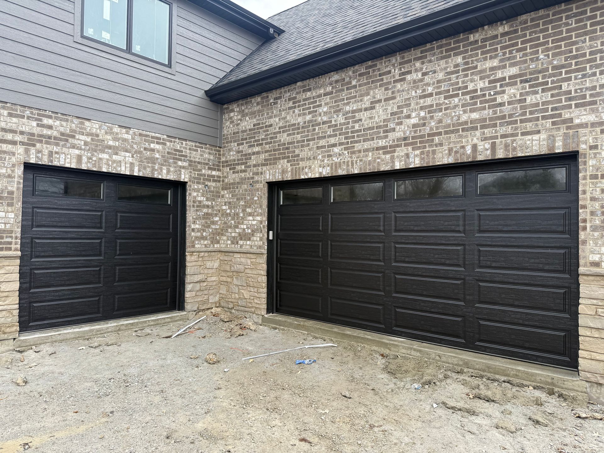 Brick house exterior with two black garage doors and a paved driveway