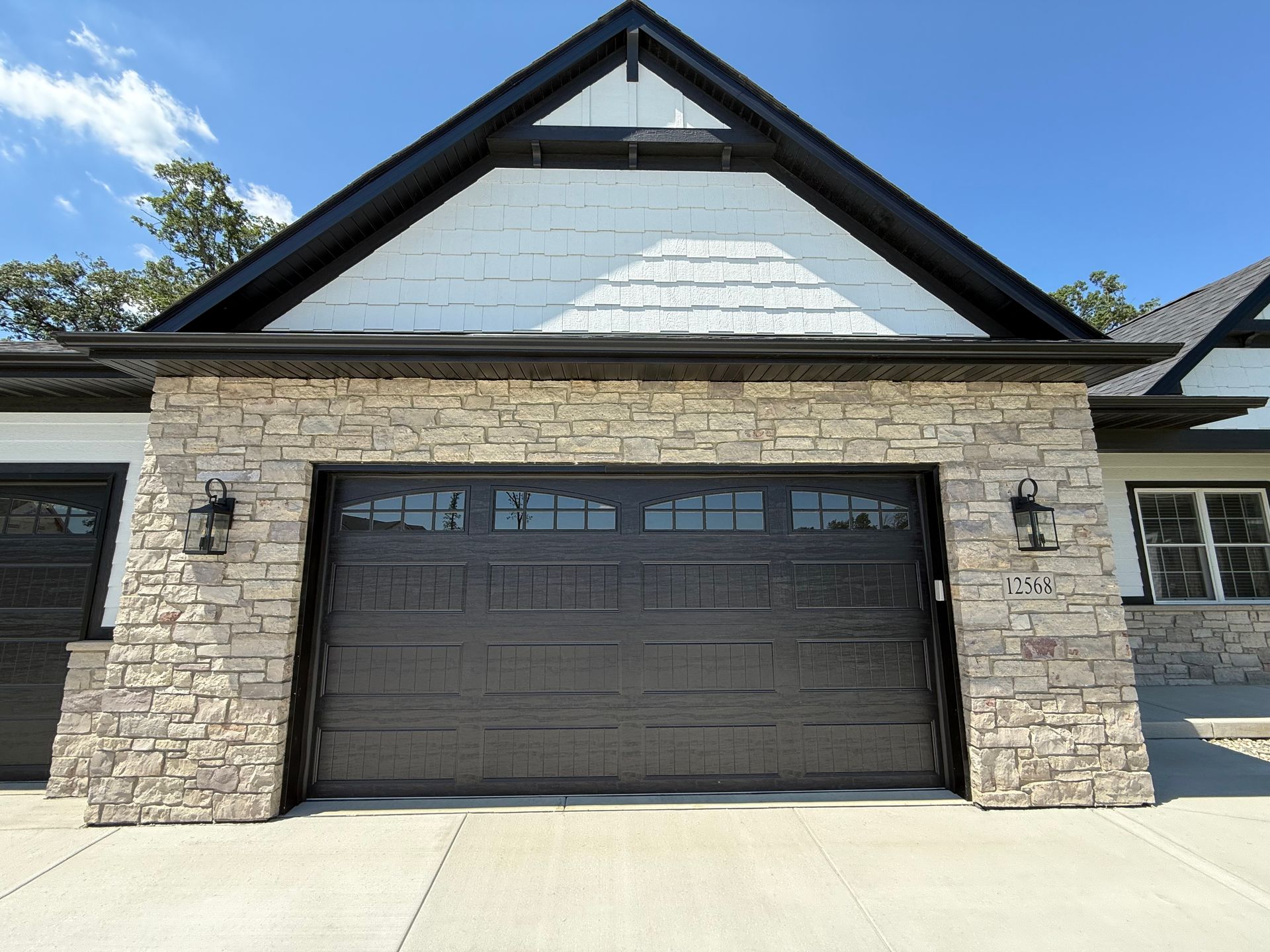 Front view of a two-car garage with stone pillars and a dark gray door under a peaked roof