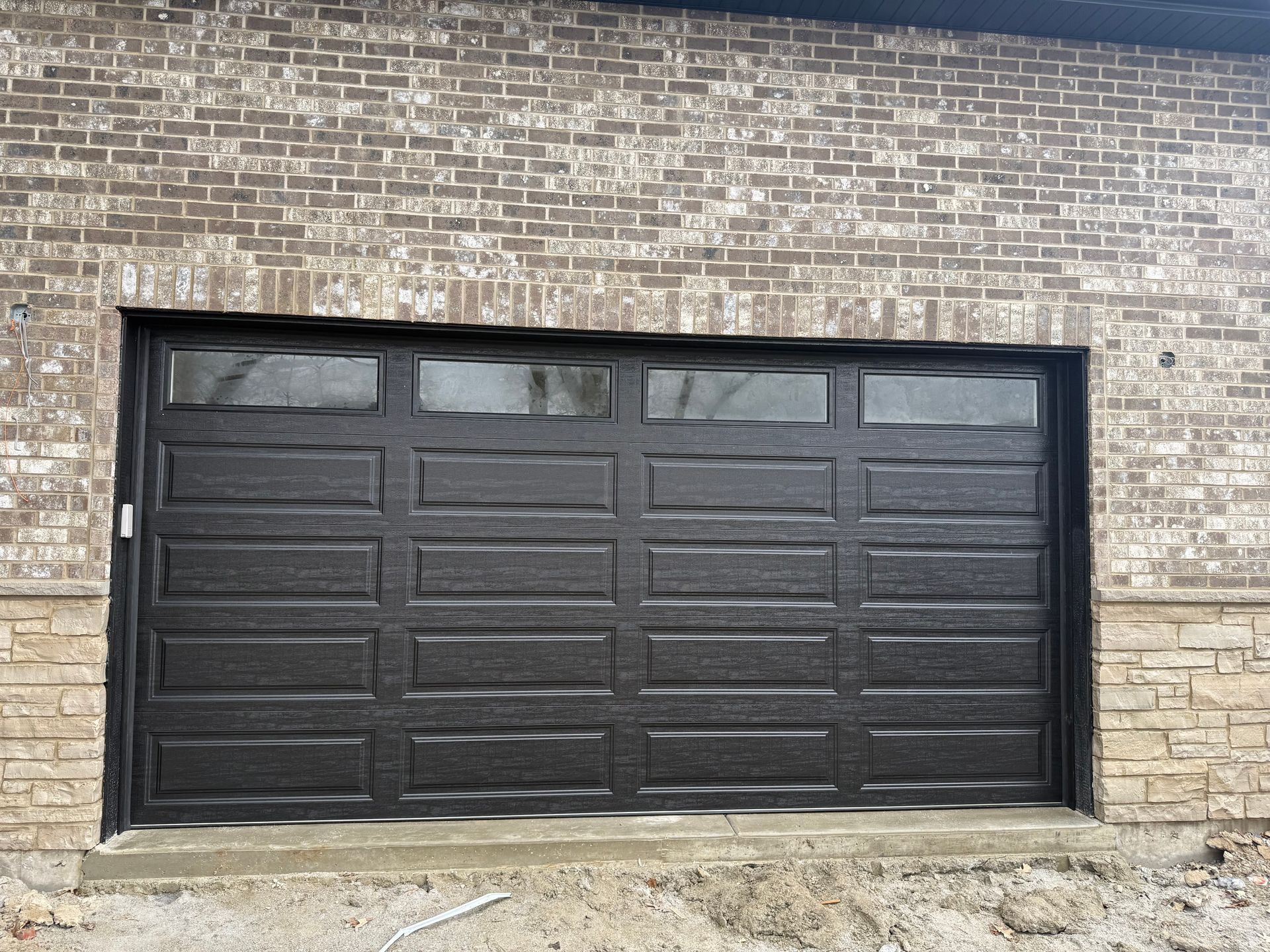 Black garage door set in a tan brick wall