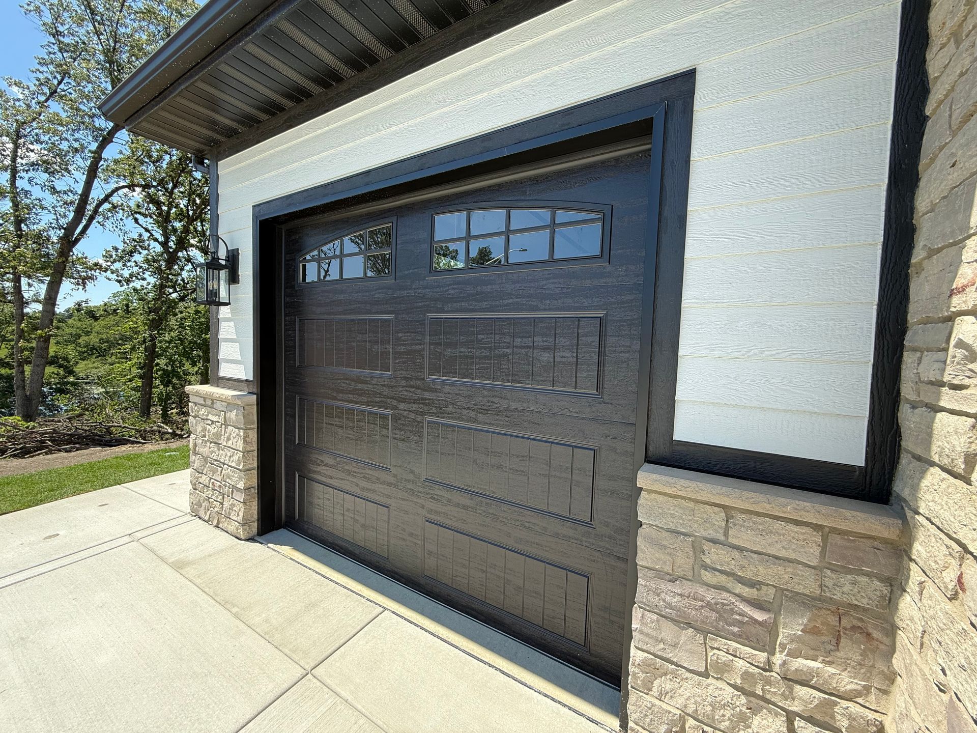 Black glass garage door on a stone-and-white exterior building in daylight