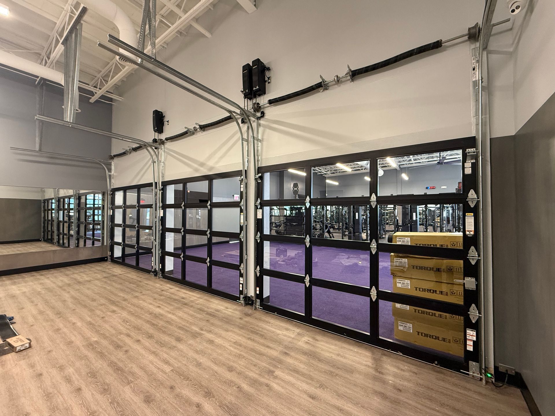 Wide indoor warehouse with glass garage doors, black shelving, and purple storage bins along one wall