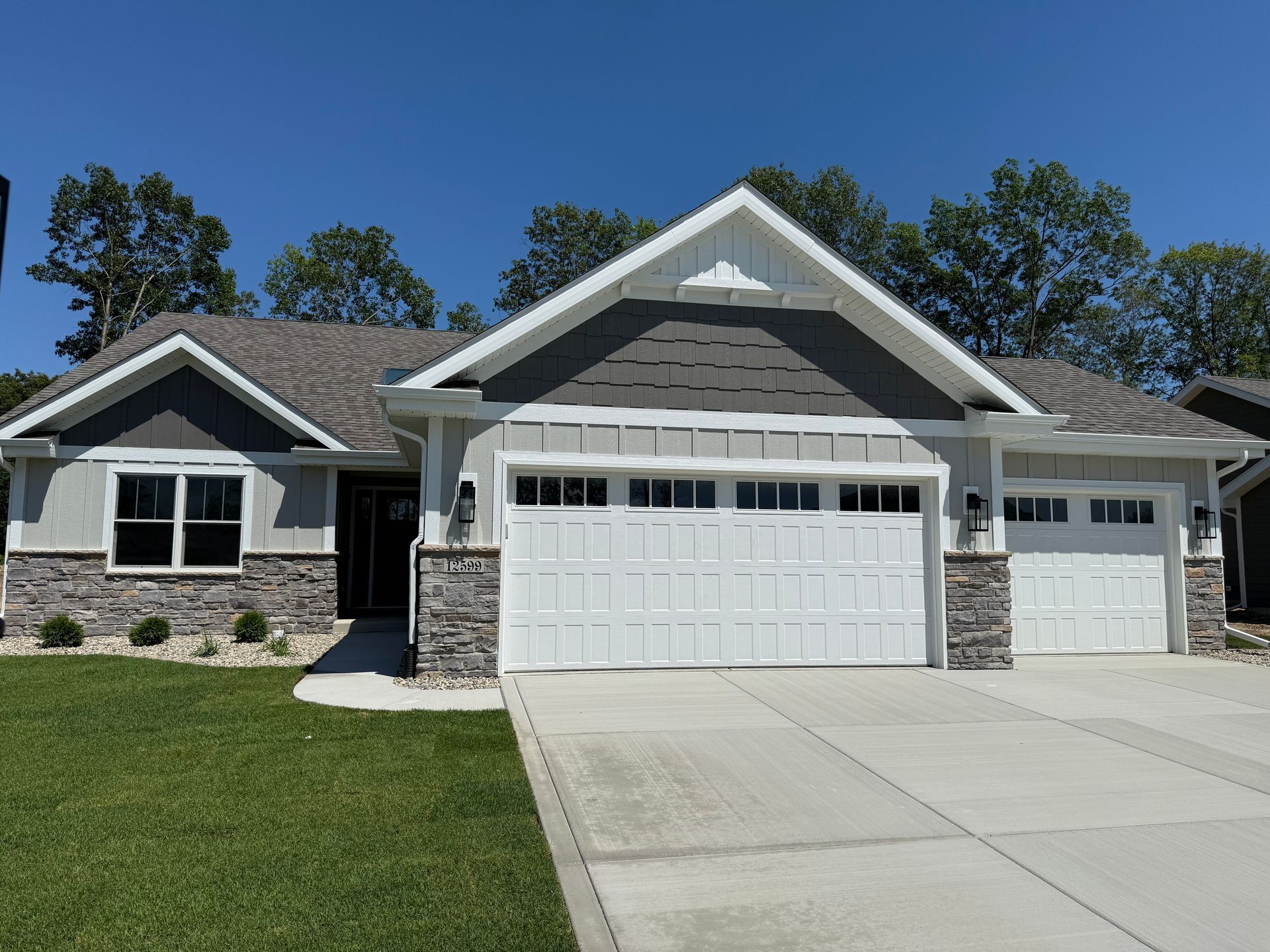 Single-story suburban house with gray stone siding, white garage doors, and a wide concrete driveway