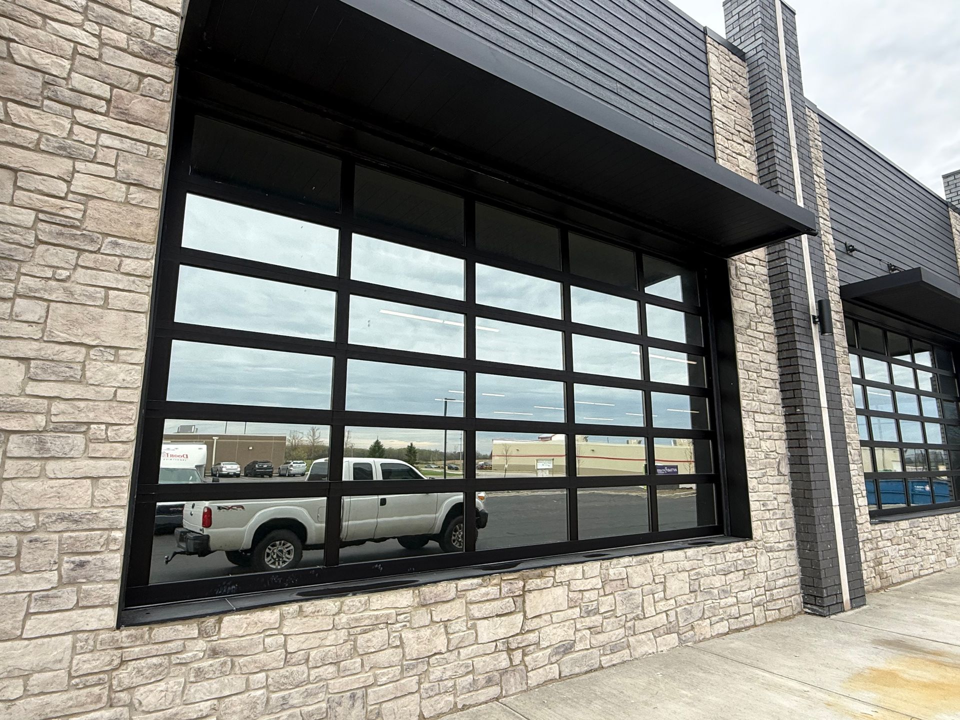 Black-framed storefront windows and stone facade reflecting a white pickup truck.