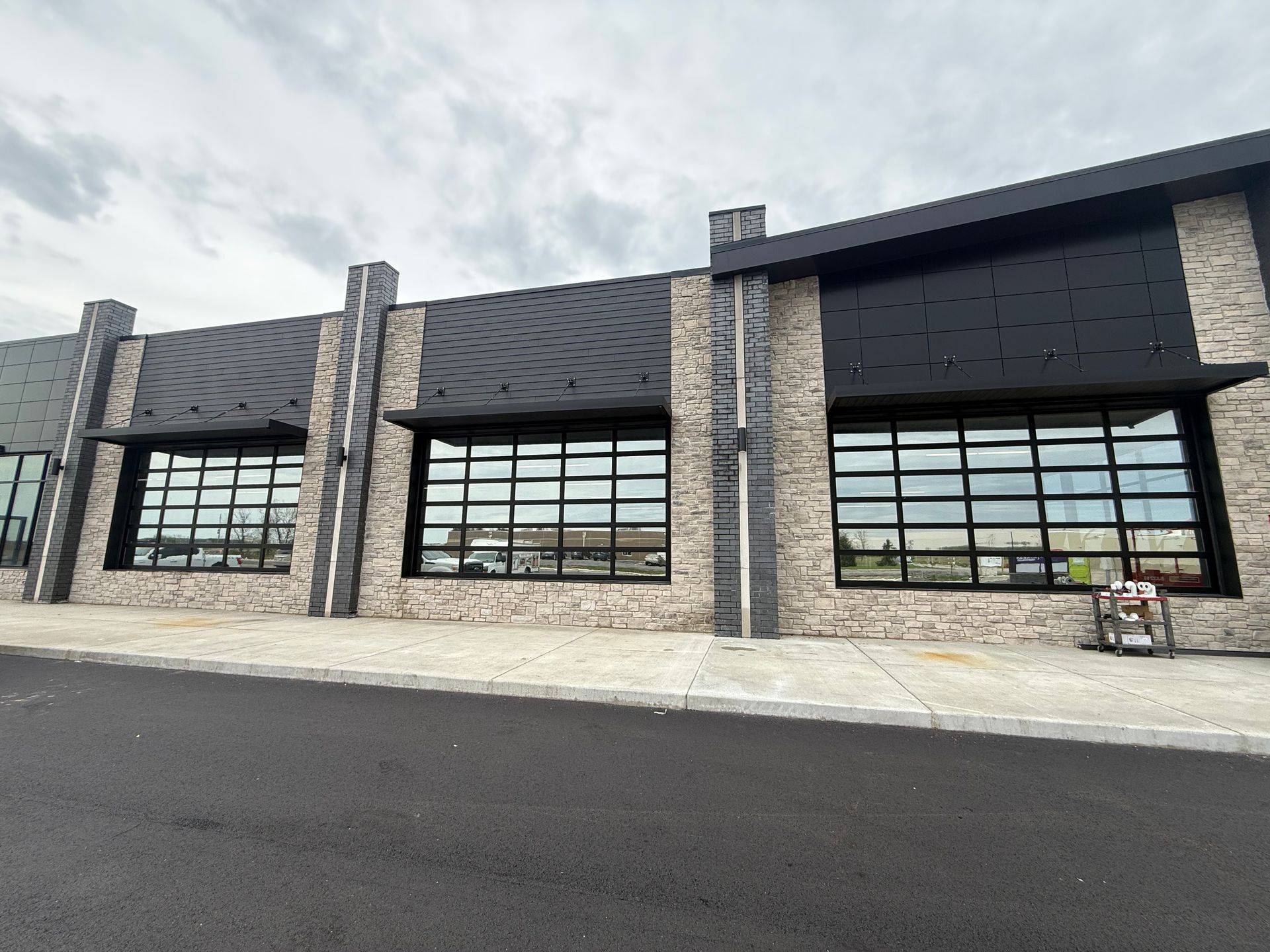 Modern commercial storefront with stone columns, large garage-style windows, and a paved parking lot