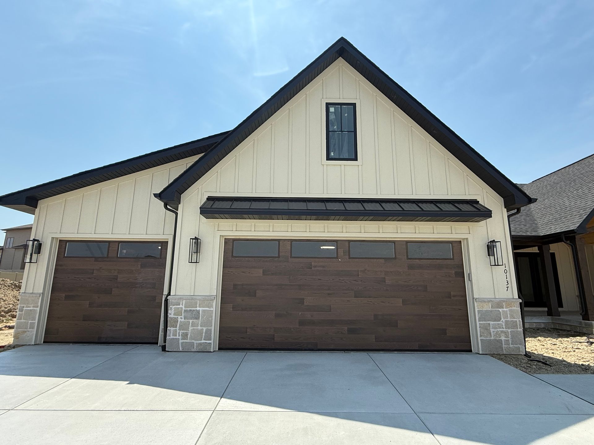 Suburban two-car garage with brown doors, beige siding, and stone accents under a blue sky