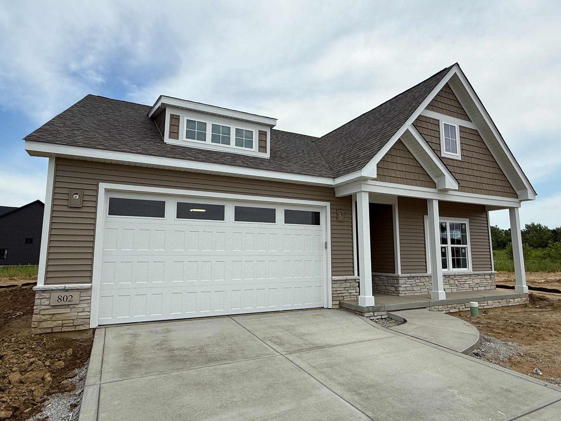New suburban house with white garage door, covered porch, and concrete driveway under construction