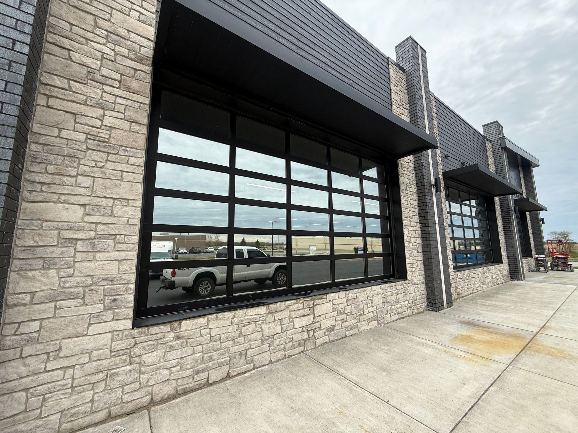 Stone storefront with large black-framed windows and a concrete sidewalk under an overcast sky