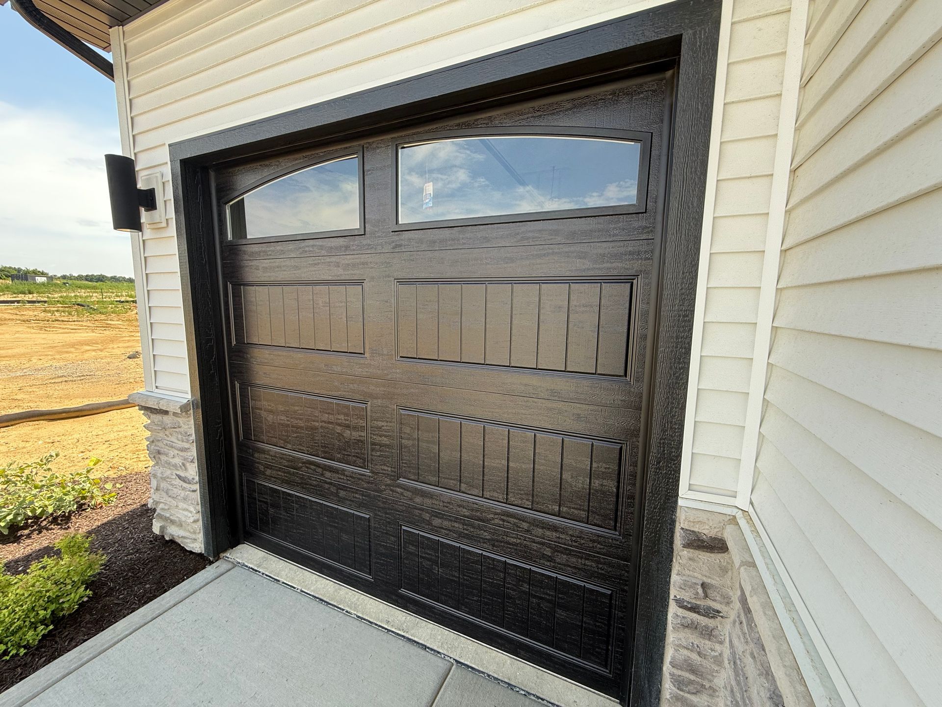 Black garage door with small window under beige siding at house entrance