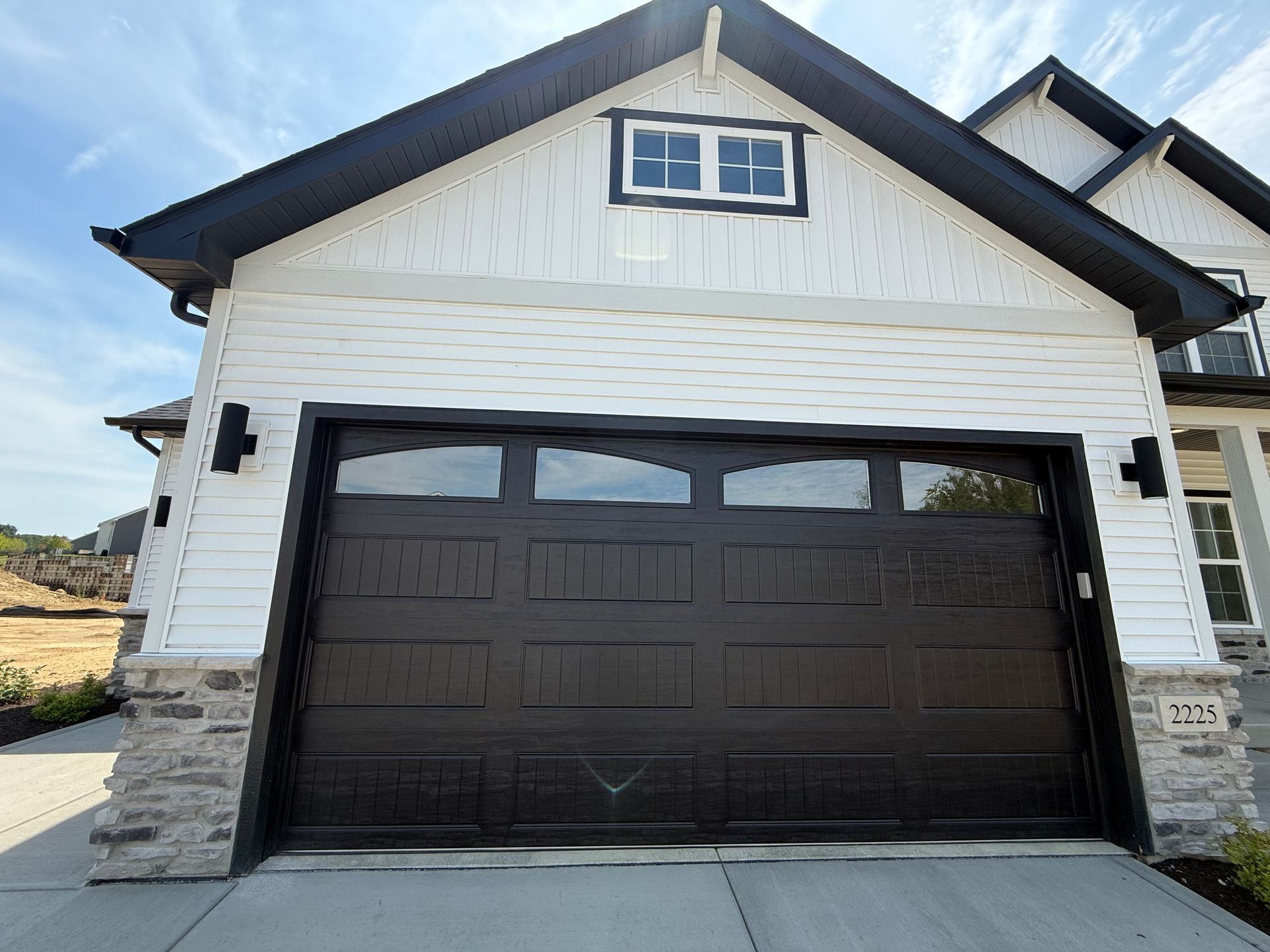 Front view of a white house with a large black garage door and stone accents
