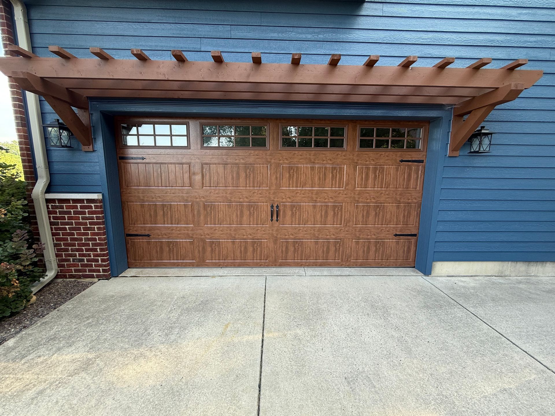 Wooden garage door with pergola overhang on a blue house beside a concrete driveway