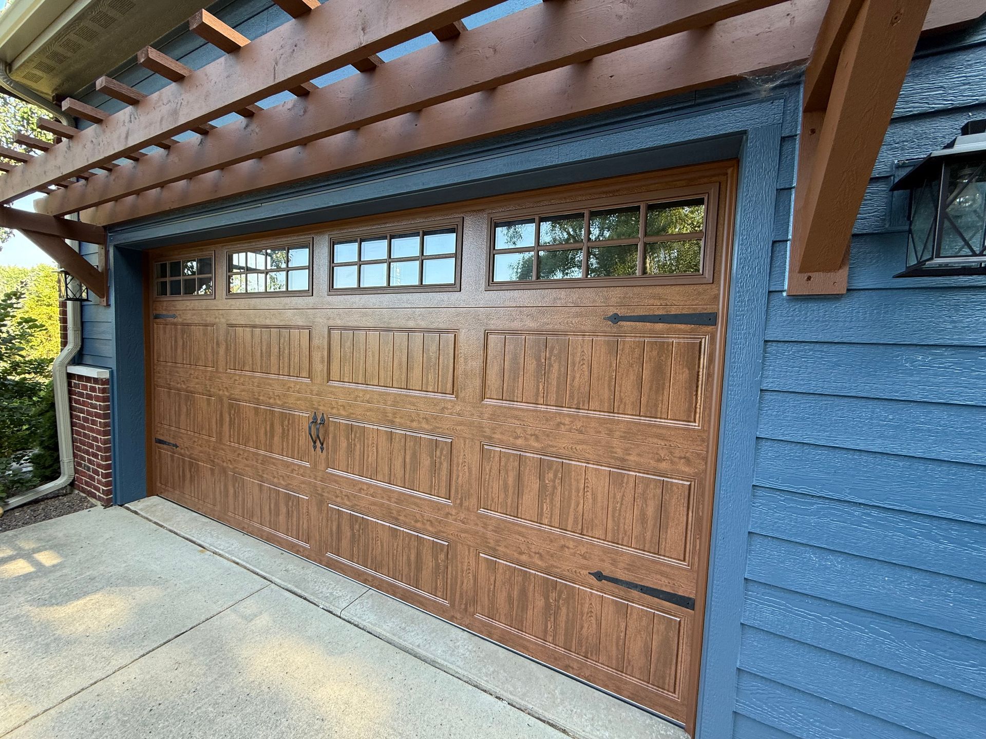 Wooden garage door with small windows beneath a blue house exterior and roof overhang