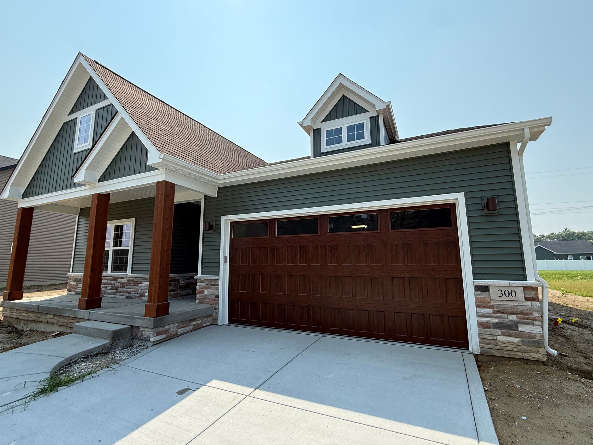 Newly built house with red garage door, white trim, and covered front porch under a clear sky
