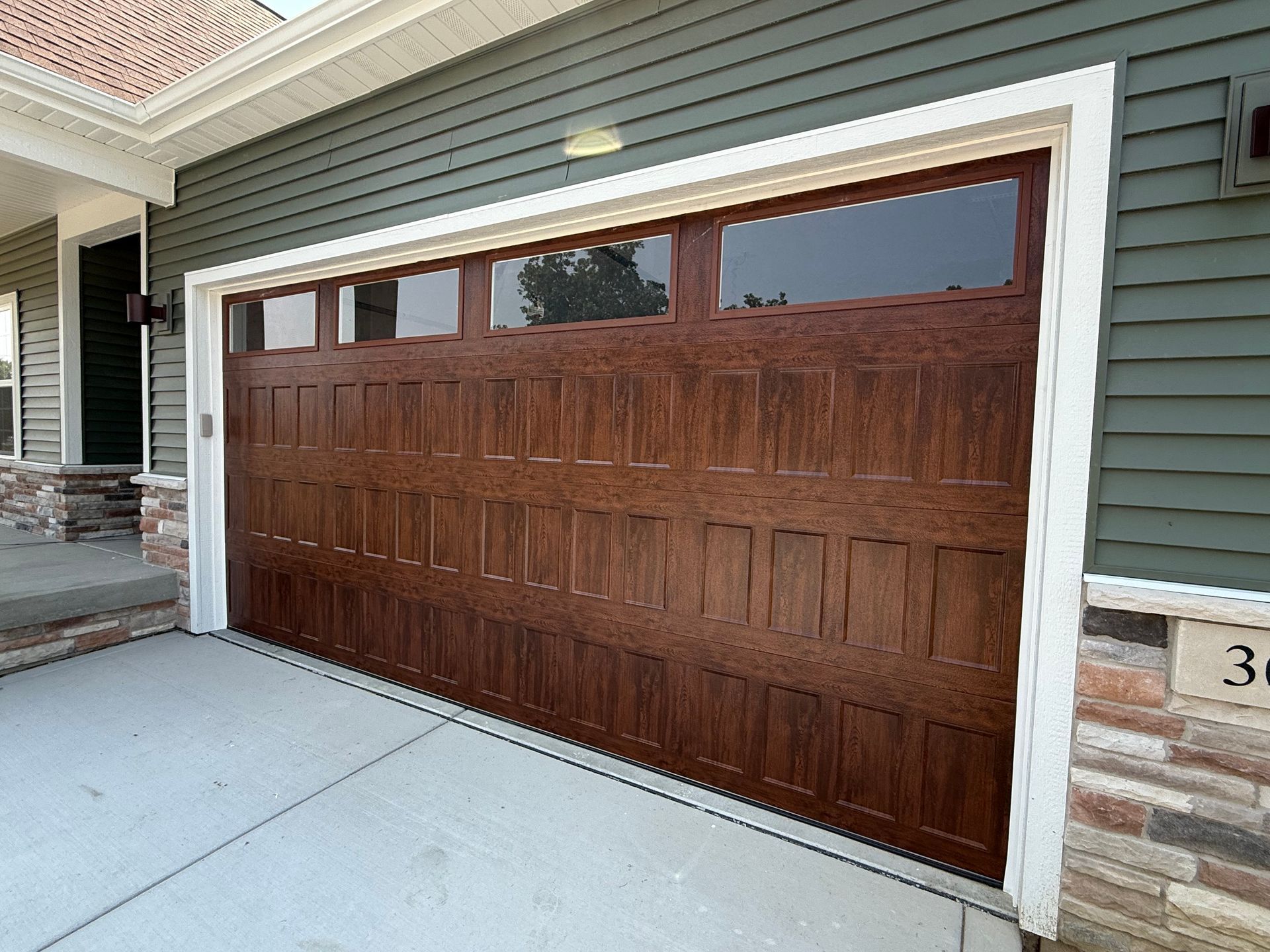 Wooden garage door with windows on a house exterior, framed by gray siding and stone trim