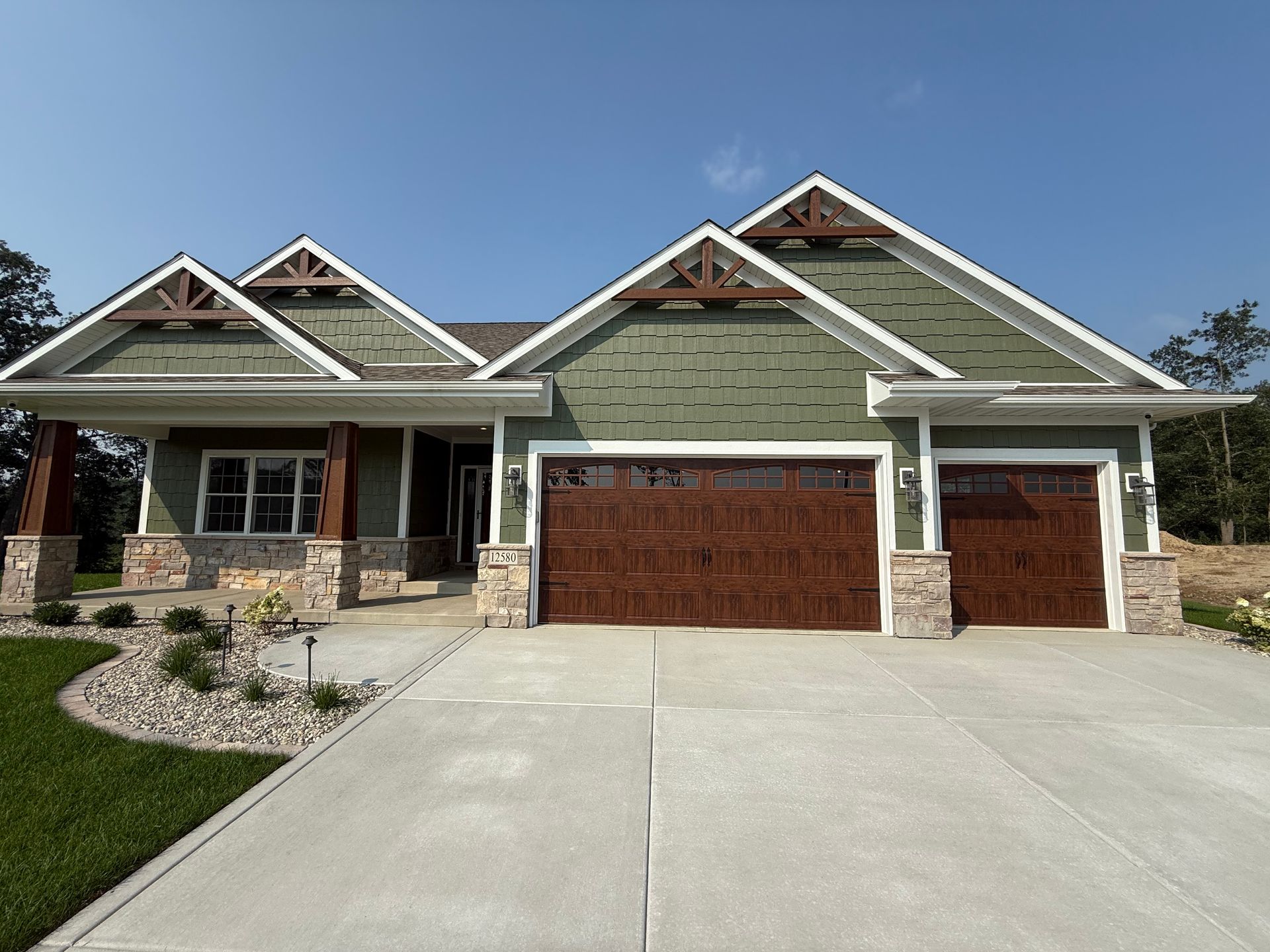 Suburban house with stone facade, green siding, two garage doors, and a wide concrete driveway